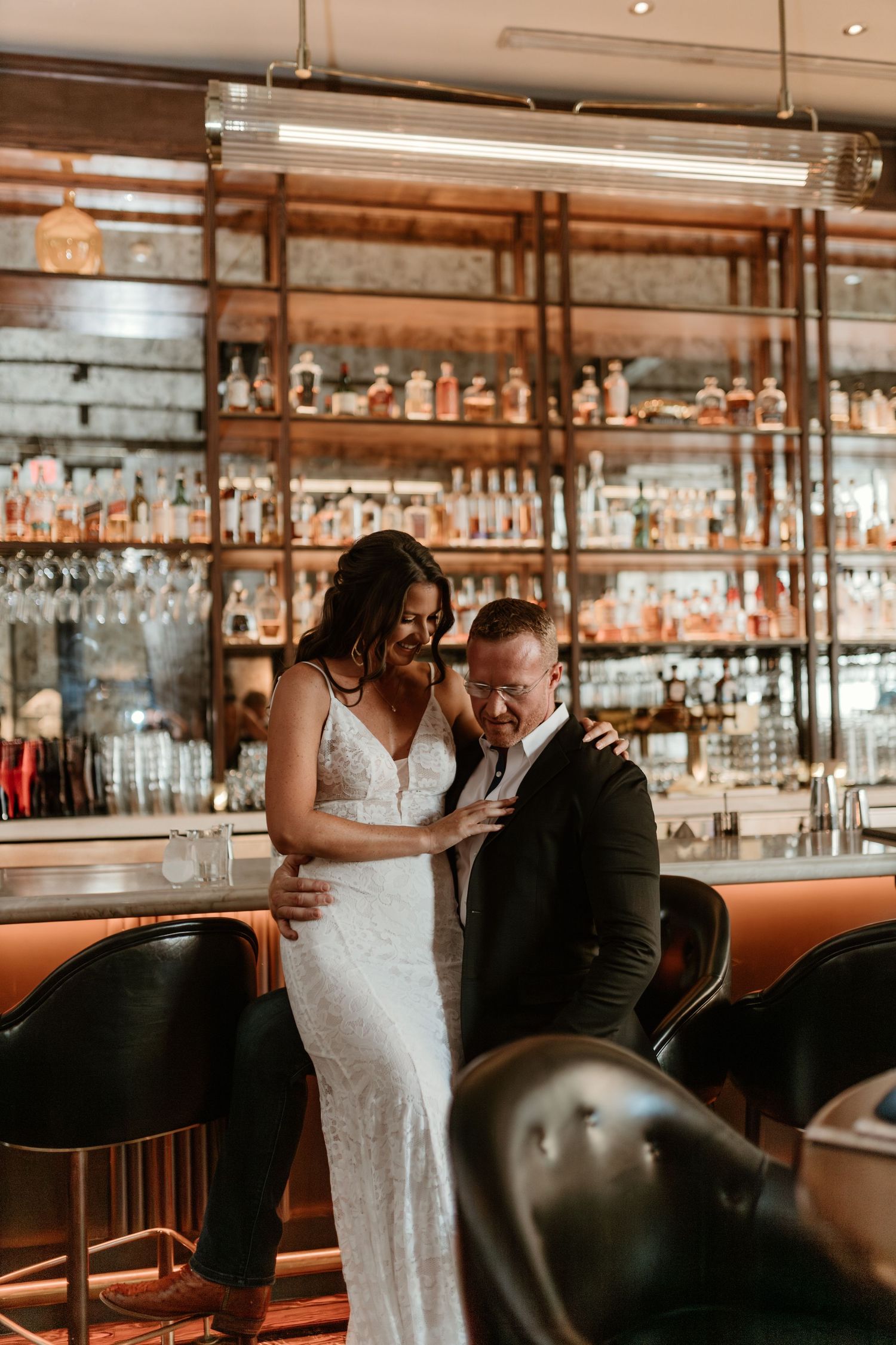 Couple shares intimate moment at stylish bar with elegant glassware and warm lighting in background.