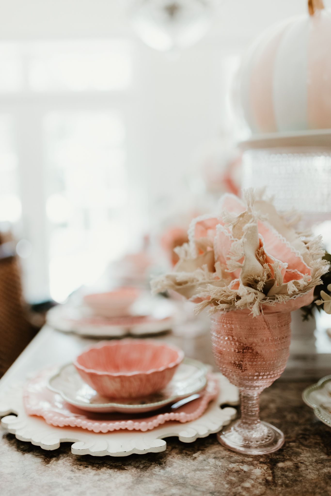 Vintage pink glass goblet and dinnerware with floral accents set on rustic table in soft natural light.