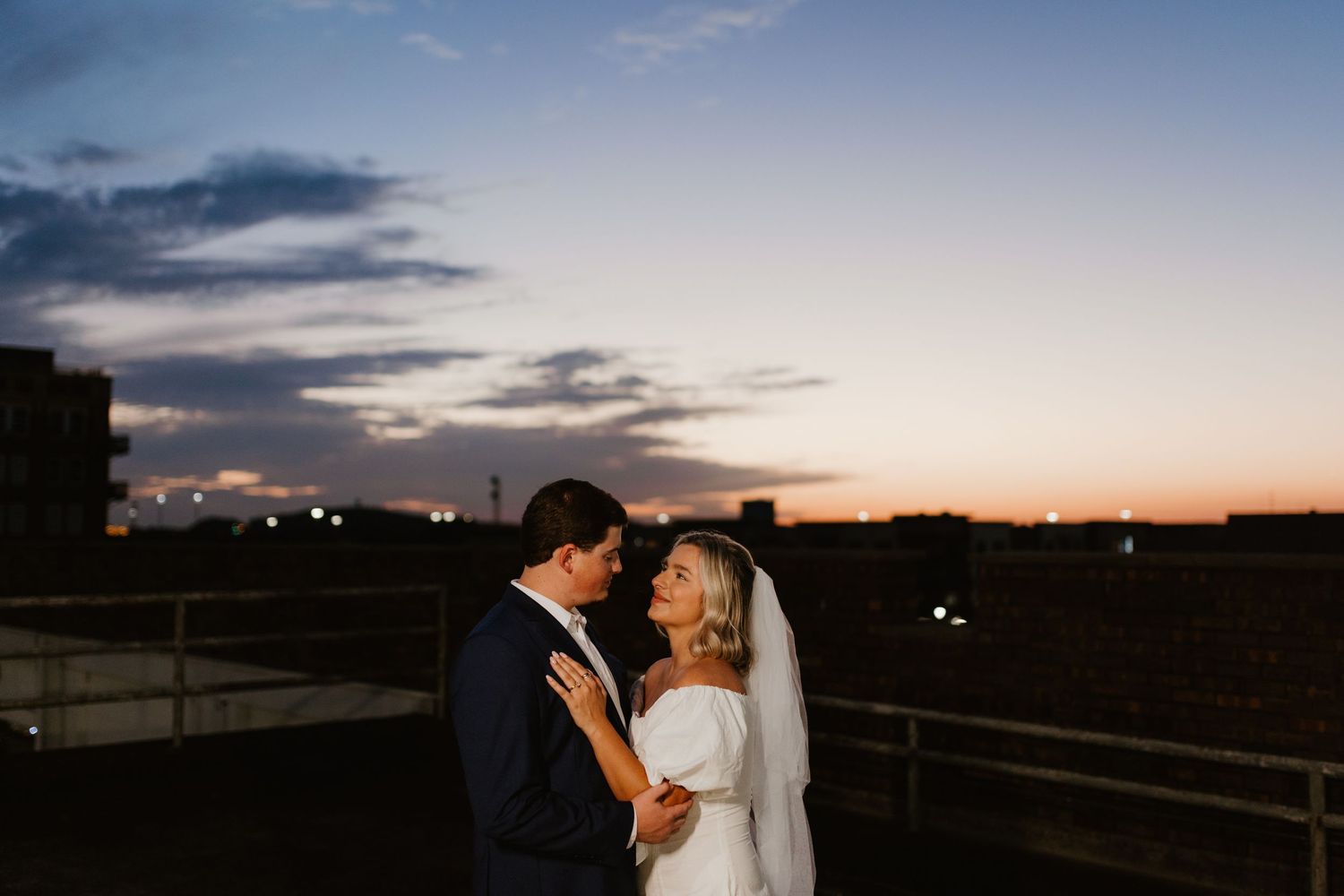 Wedding couple embraces during sunset as dramatic clouds fill the sky over a scenic outdoor landscape.