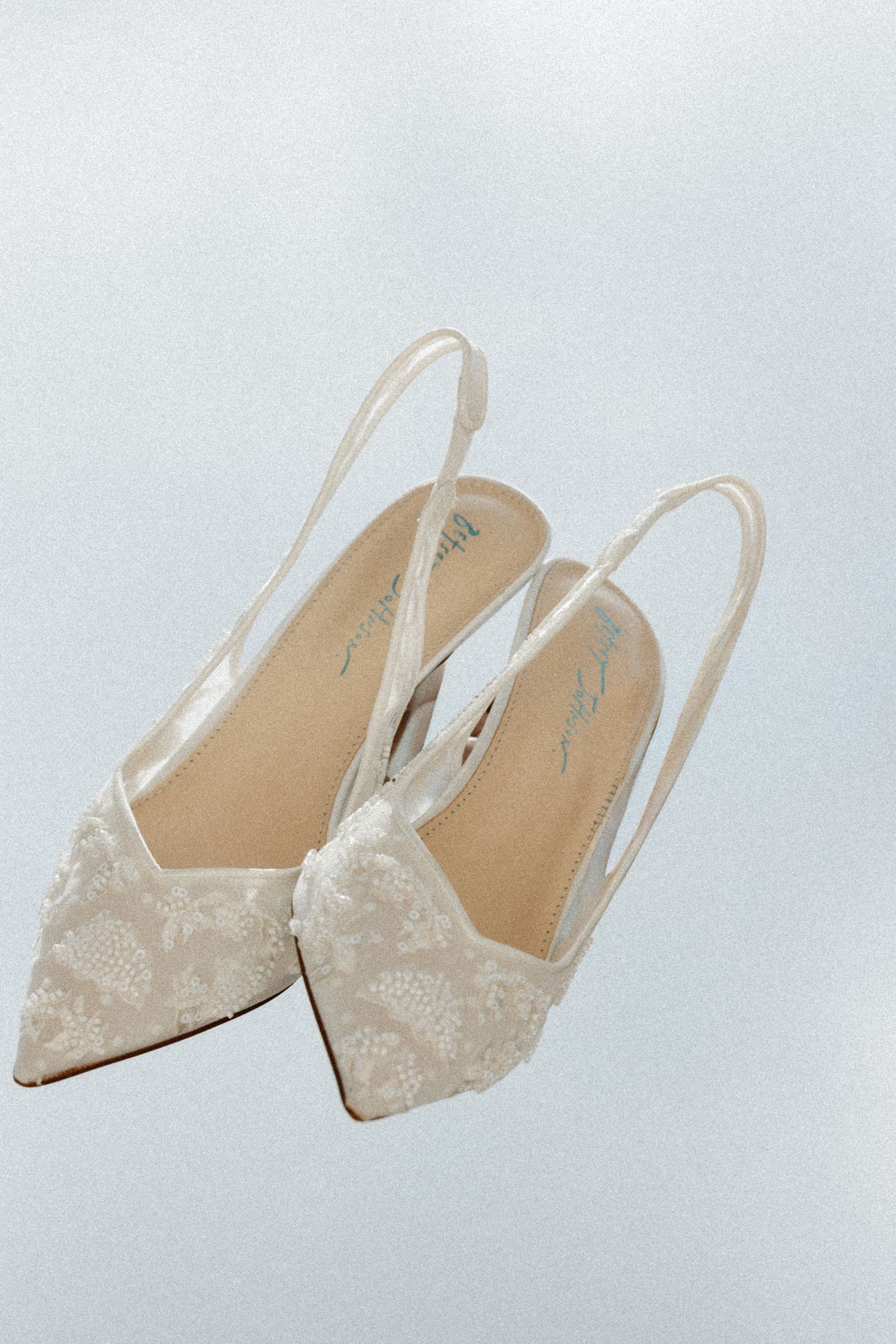 Elegant ivory lace slingback pointed-toe wedding heels with floral detailing on a soft white background.