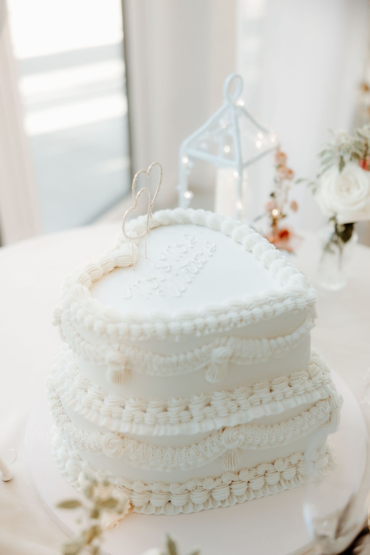 Elegant two-tier heart-shaped white wedding cake decorated with pearl borders and floral details.