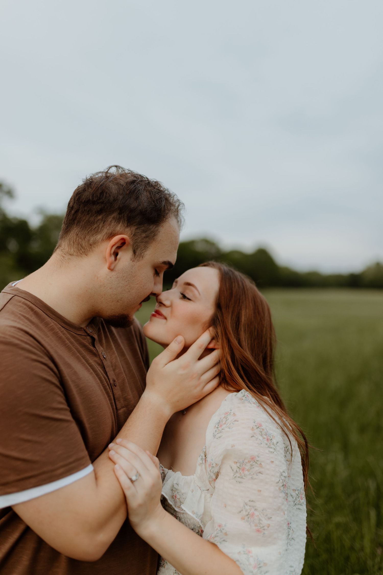 Romantic couple sharing an intimate moment in a green field, man tenderly holding womans face as they lean in for a kiss.
