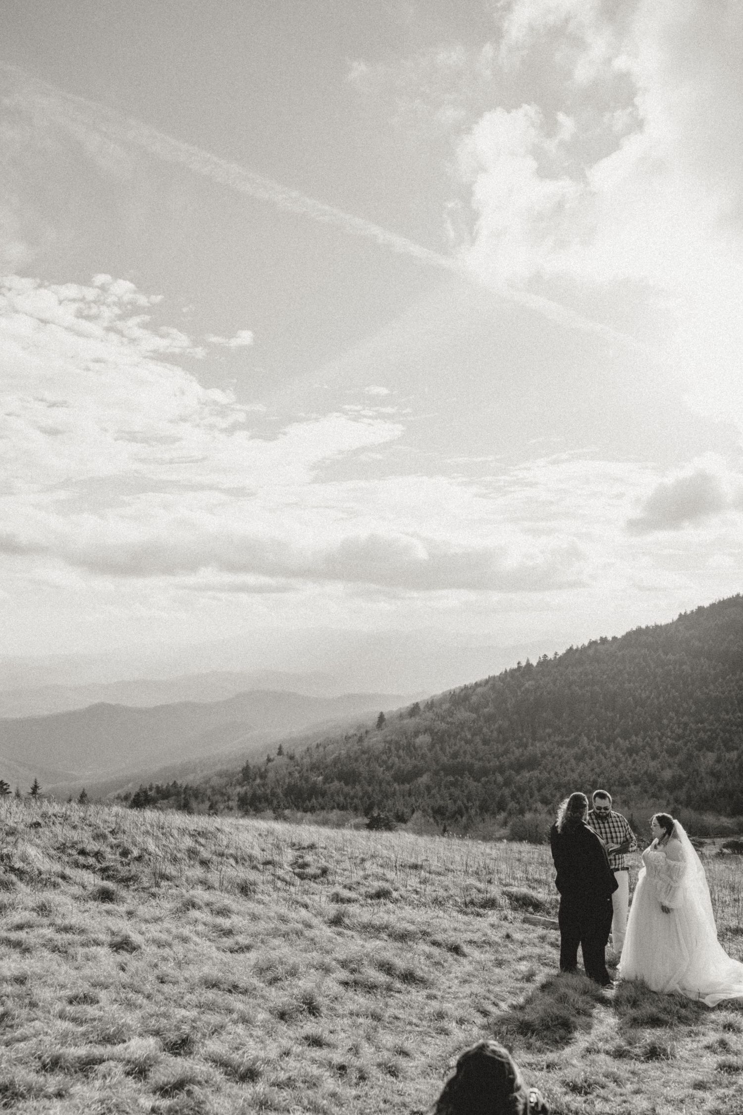 Black and white photo of couple exchanging vows on mountain hilltop with scenic valley views.