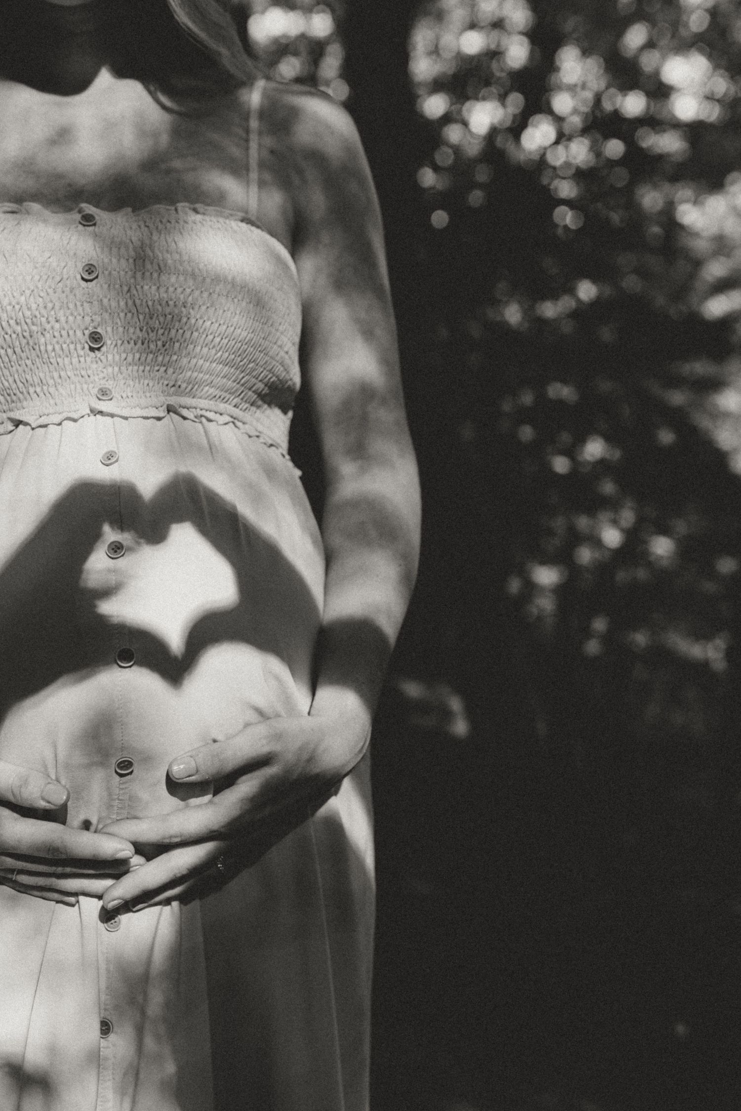 Black and white photo showing hands forming heart shape over pregnant belly.