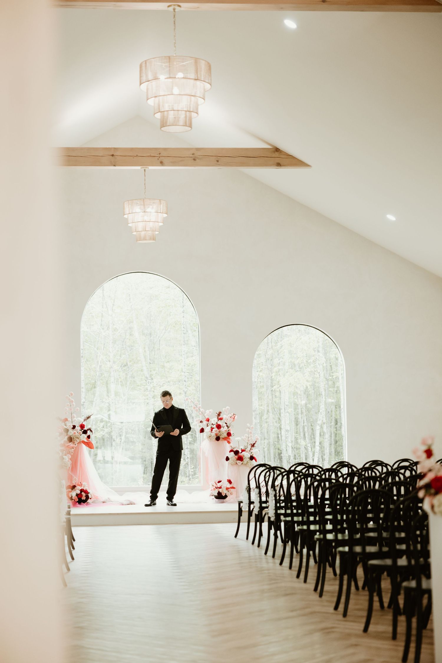 Modern white chapel interior with black chairs and pink floral arrangements by arched windows.