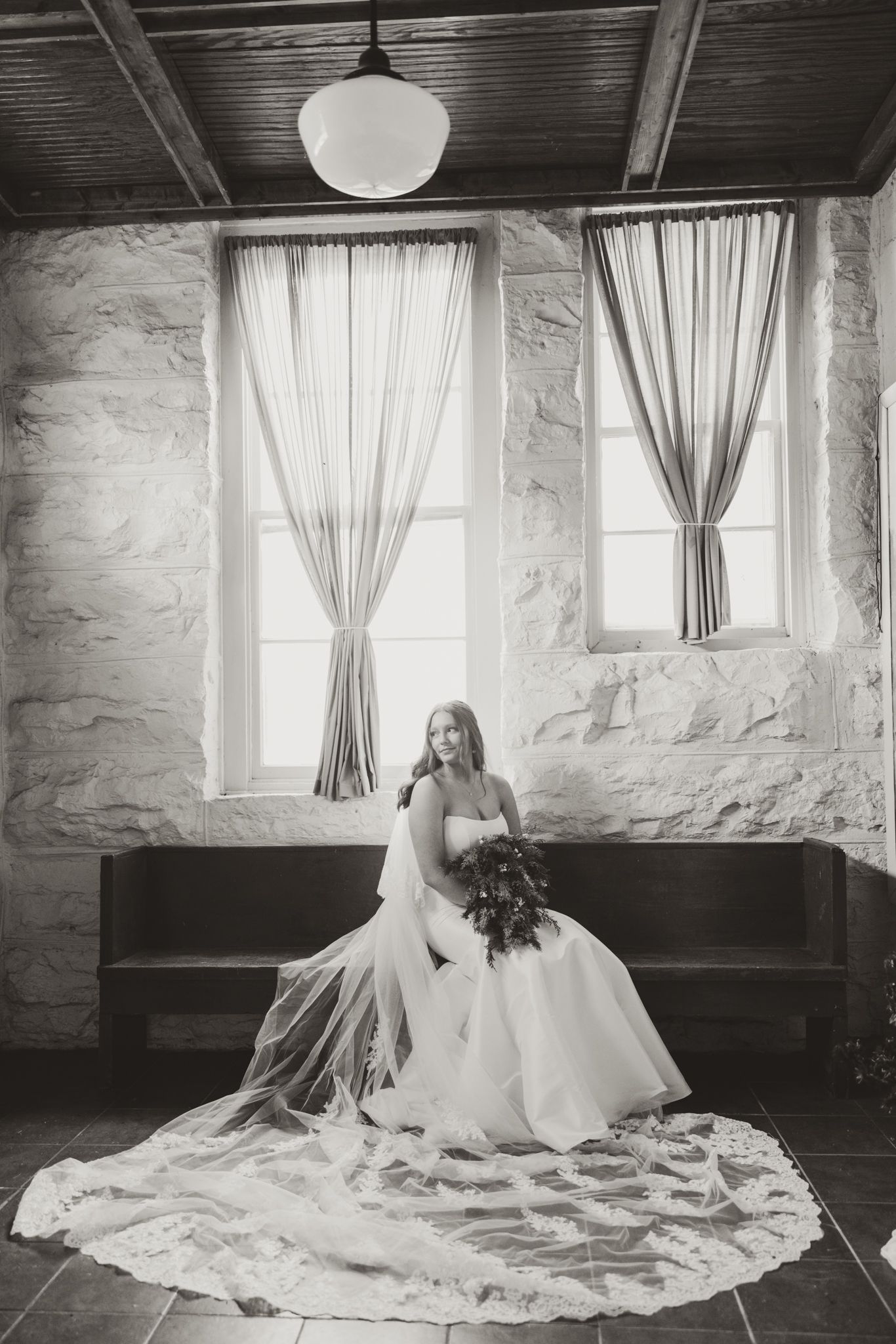 Black and white bridal portrait in a rustic room with flowing curtains and stone walls.