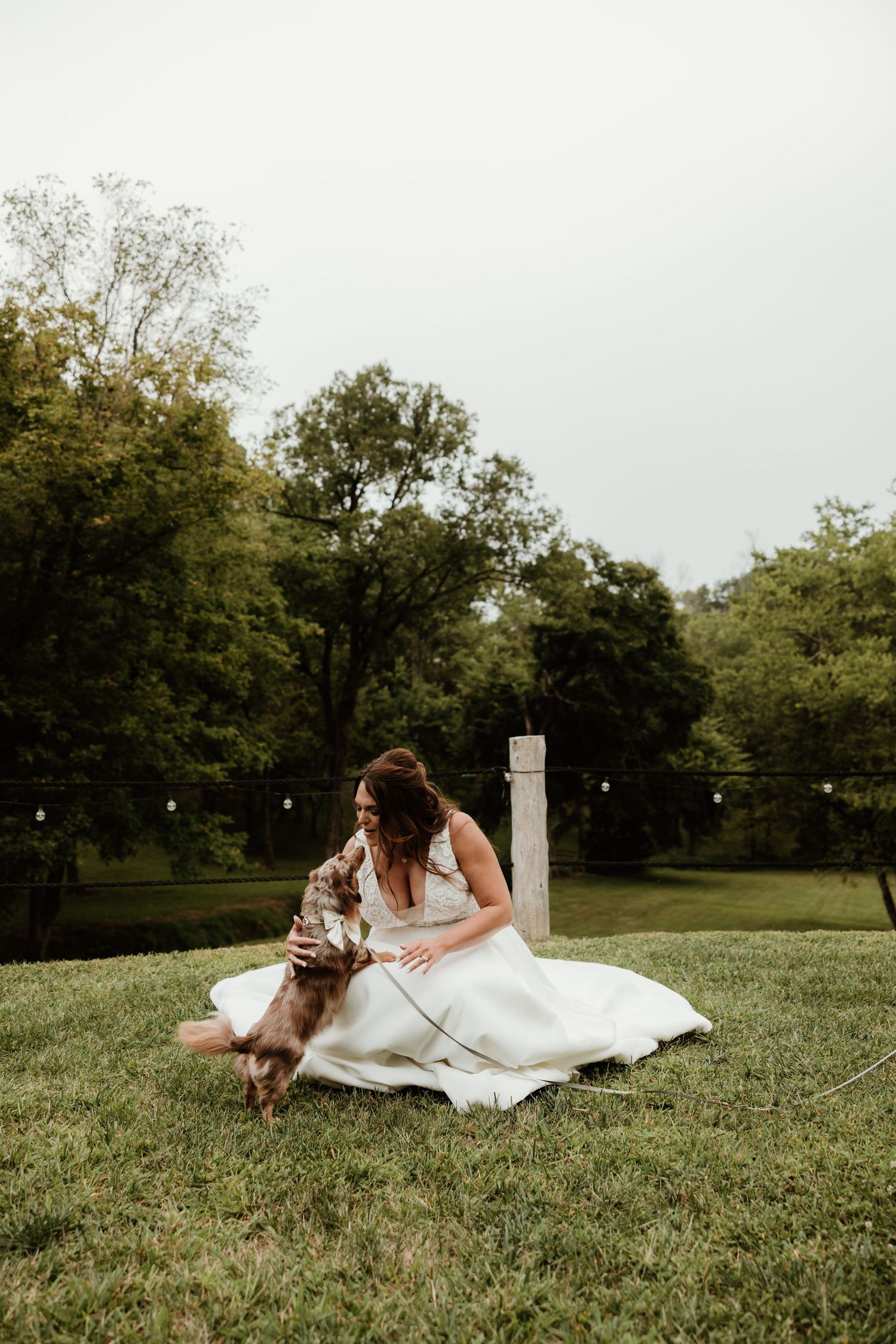 Couple shares tender moments on grassy lawn with their dog during wedding photoshoot.