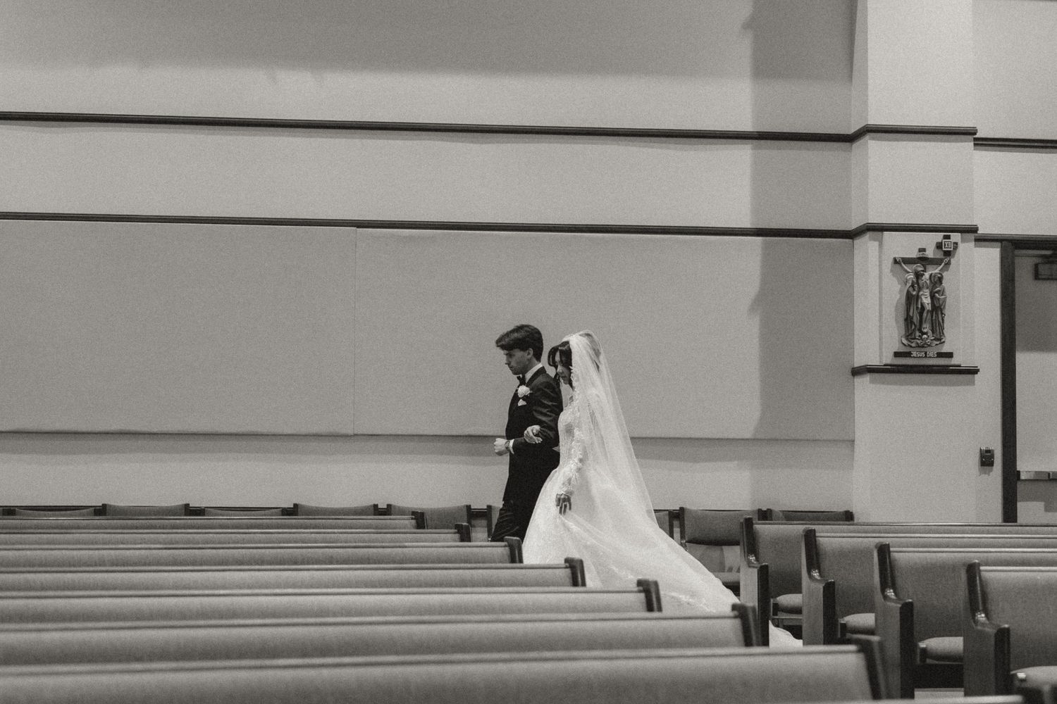 Black and white photo of a bride and groom walking down the aisle of a church on their wedding day.