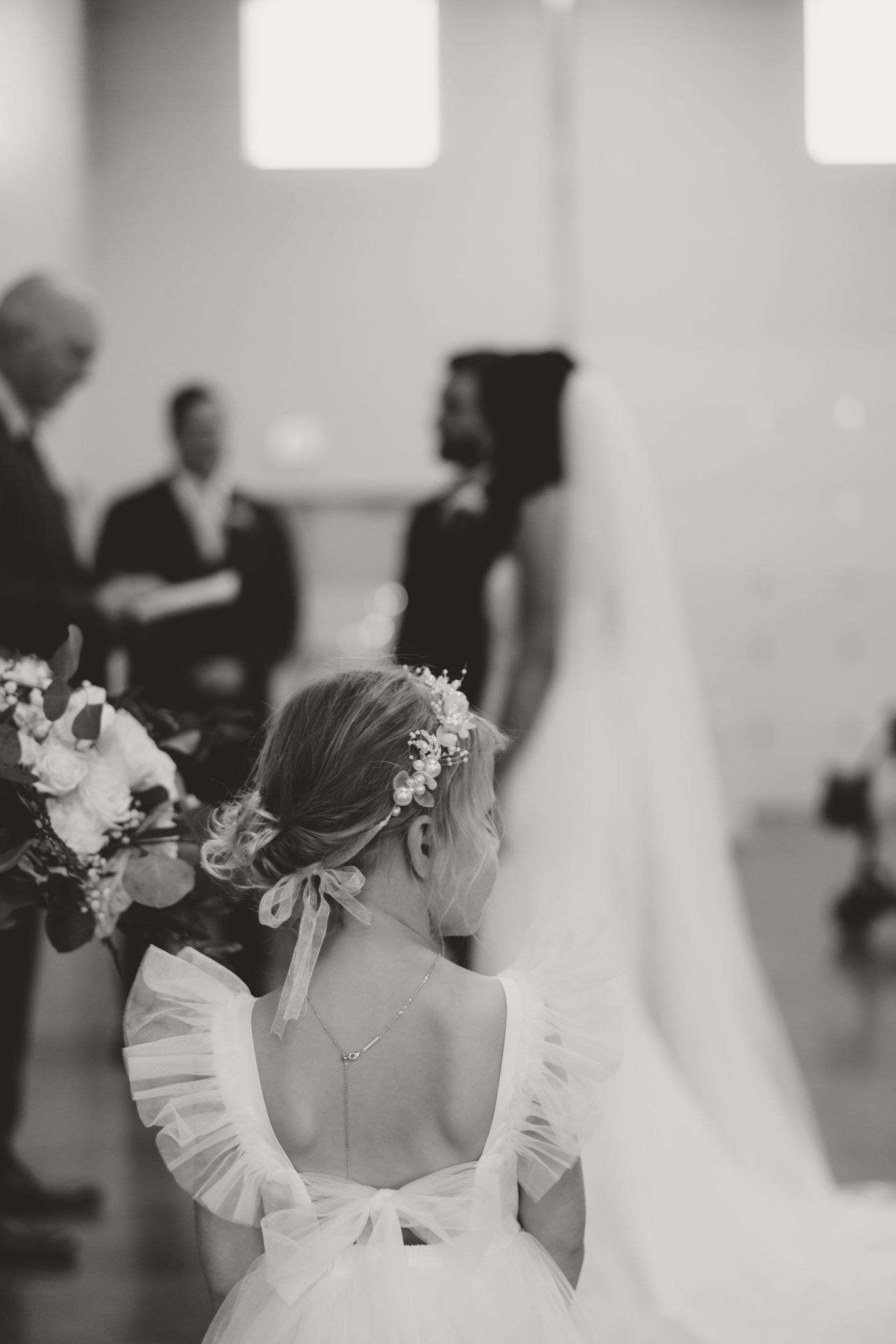 Black and white photo of a bride in a white wedding dress with floral details viewed from behind.