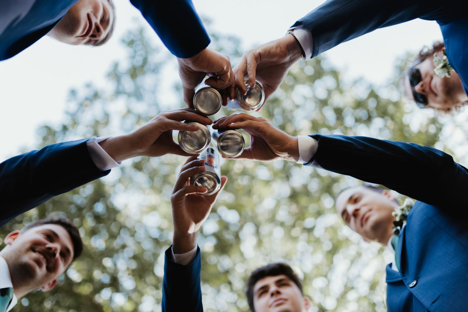 Low angle view of friends toasting and clinking wine glasses together outdoors with blurred trees in background.