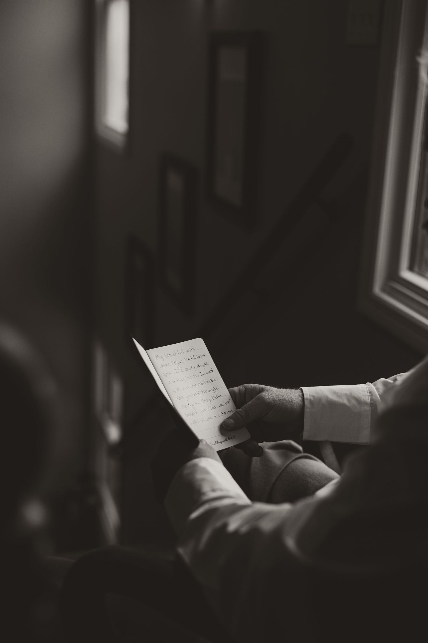 Hands holding a letter in shadows, silhouetted against window light in a dramatic black and white composition.