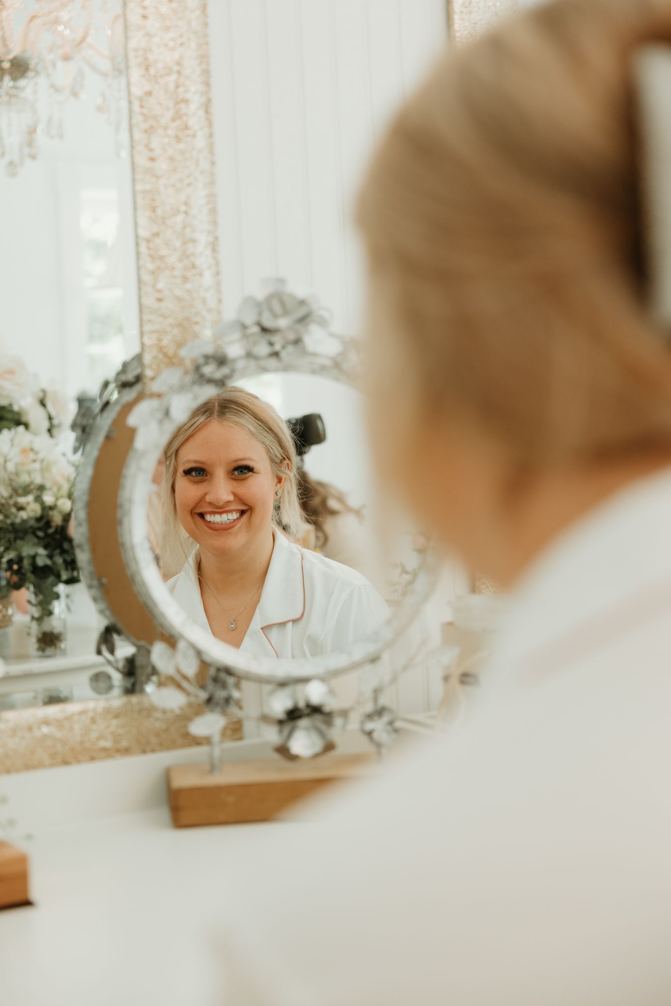 A reflection in a decorative mirror shows a person wearing white getting ready for a special occasion.