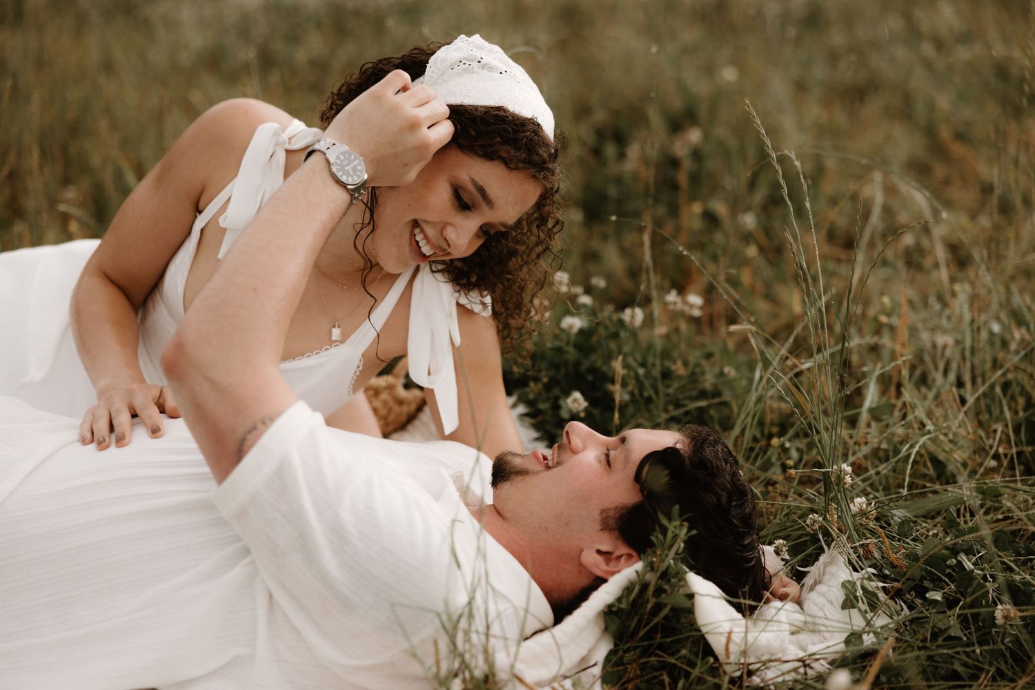 A romantic wedding couple lies together in a wildflower meadow during a sunset photoshoot.