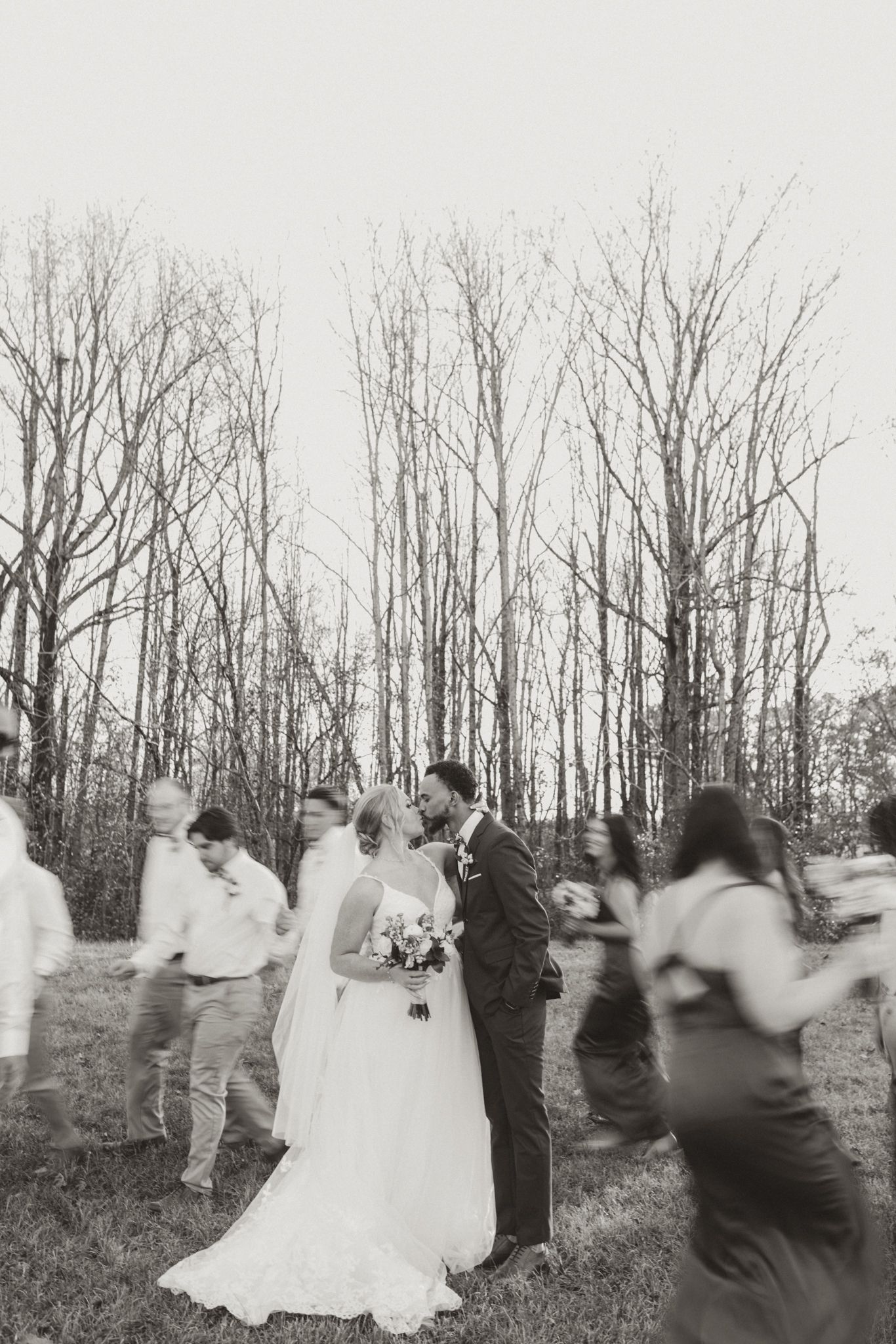 Motion-blurred black and white photo of wedding guests celebrating around the newlyweds.