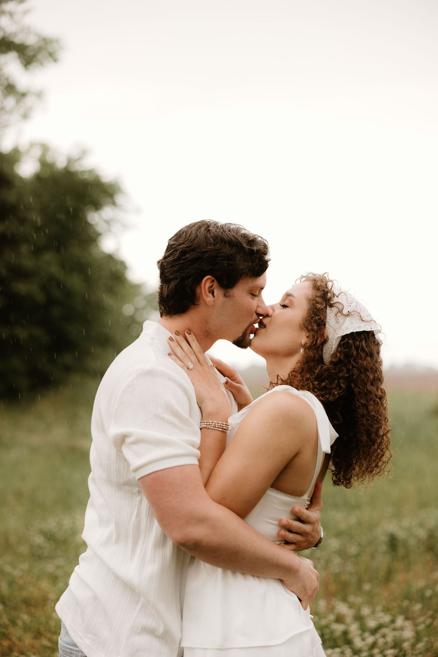 Romantic embrace between couple wearing all white in a summer meadow.