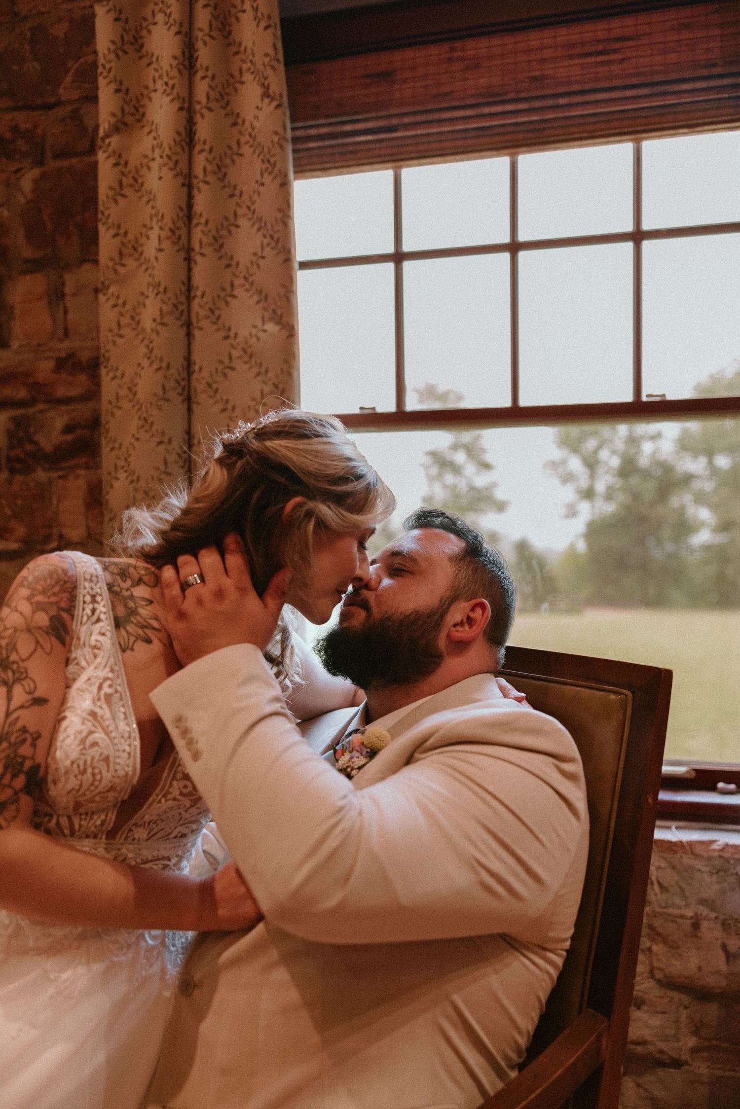 Intimate wedding moment captured by window in rustic stone building with natural light.