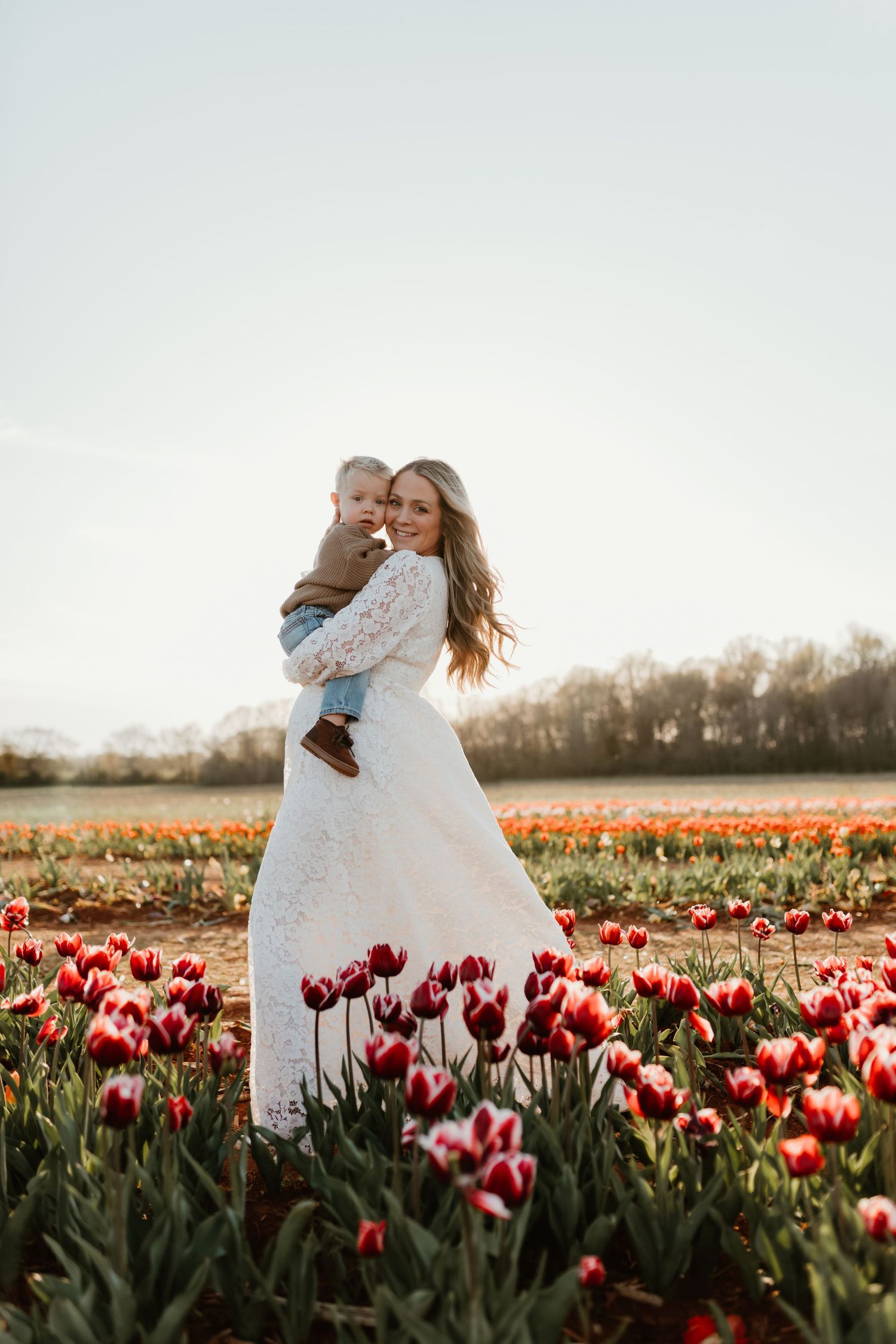 Couple embraces joyfully in a vibrant field of red and white tulips during spring.