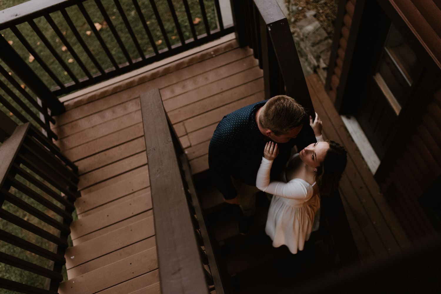 A couple embracing on a wooden deck staircase viewed from above.