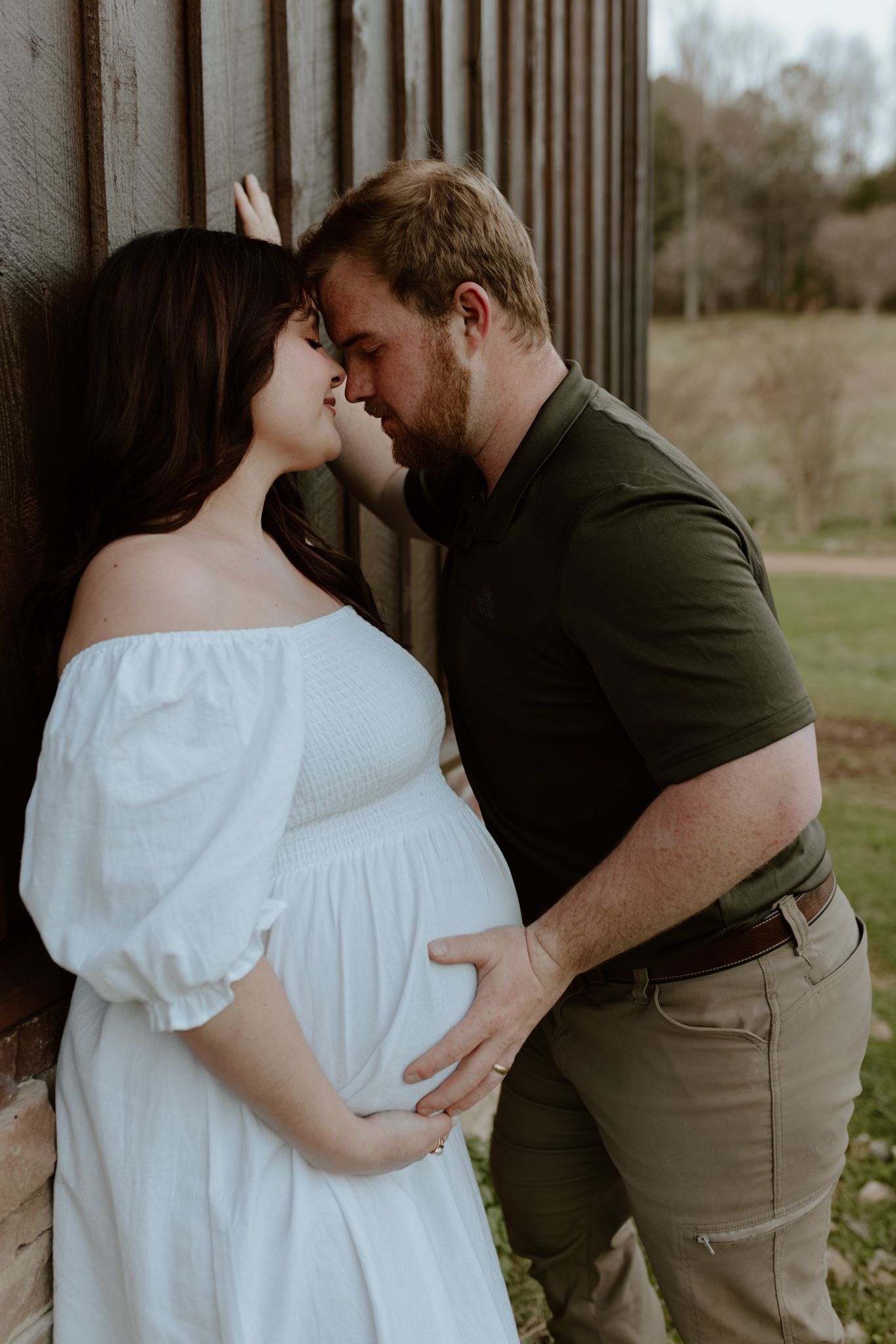 A tender intimate moment between a couple in white dress and green shirt against a rustic wooden wall.