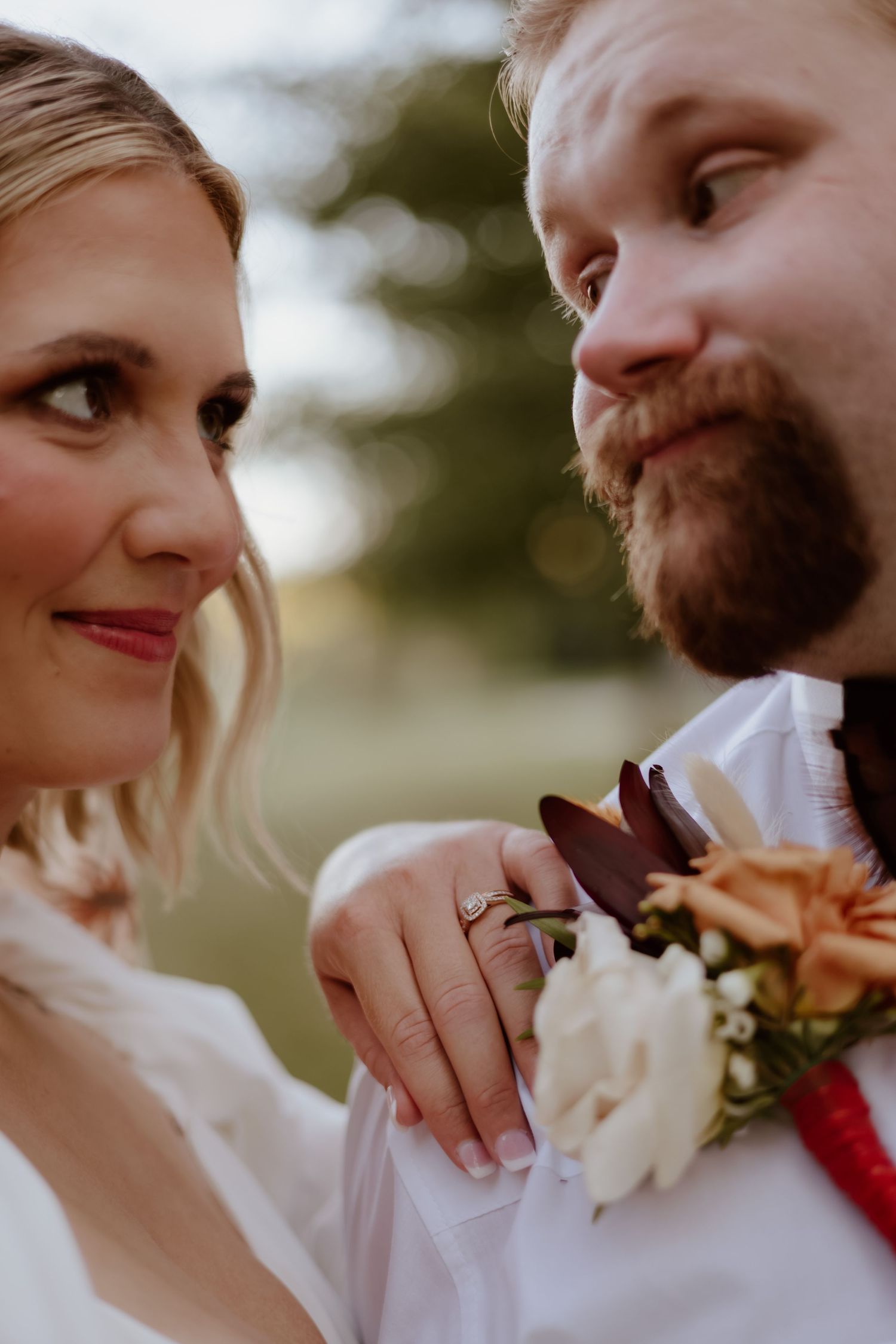 Close-up shot of couple on their wedding day with white dress, beard, and floral boutonniere in soft natural light.