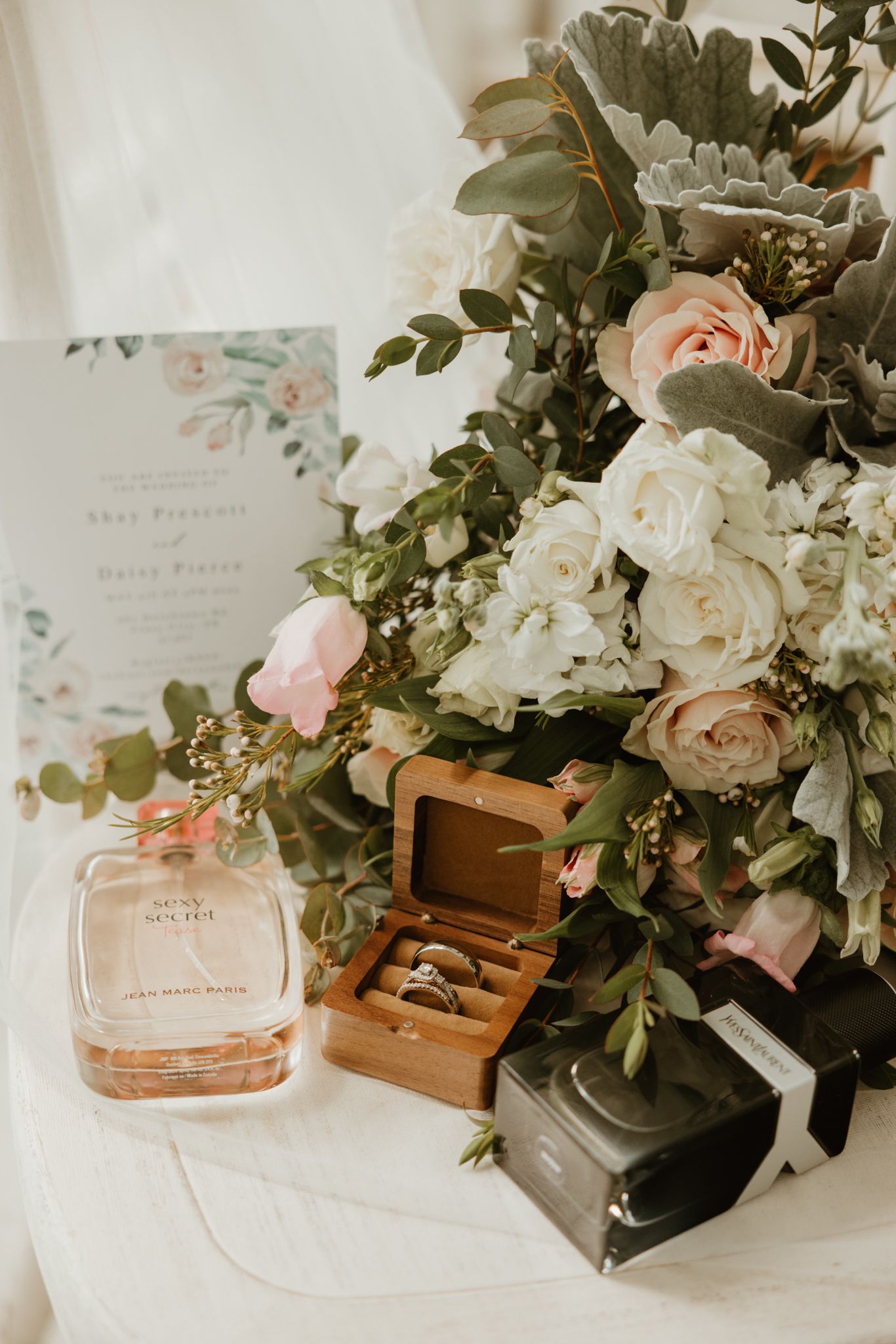 Wedding details including floral arrangements with blush roses, eucalyptus greenery, and perfume bottles displayed on a white surface.