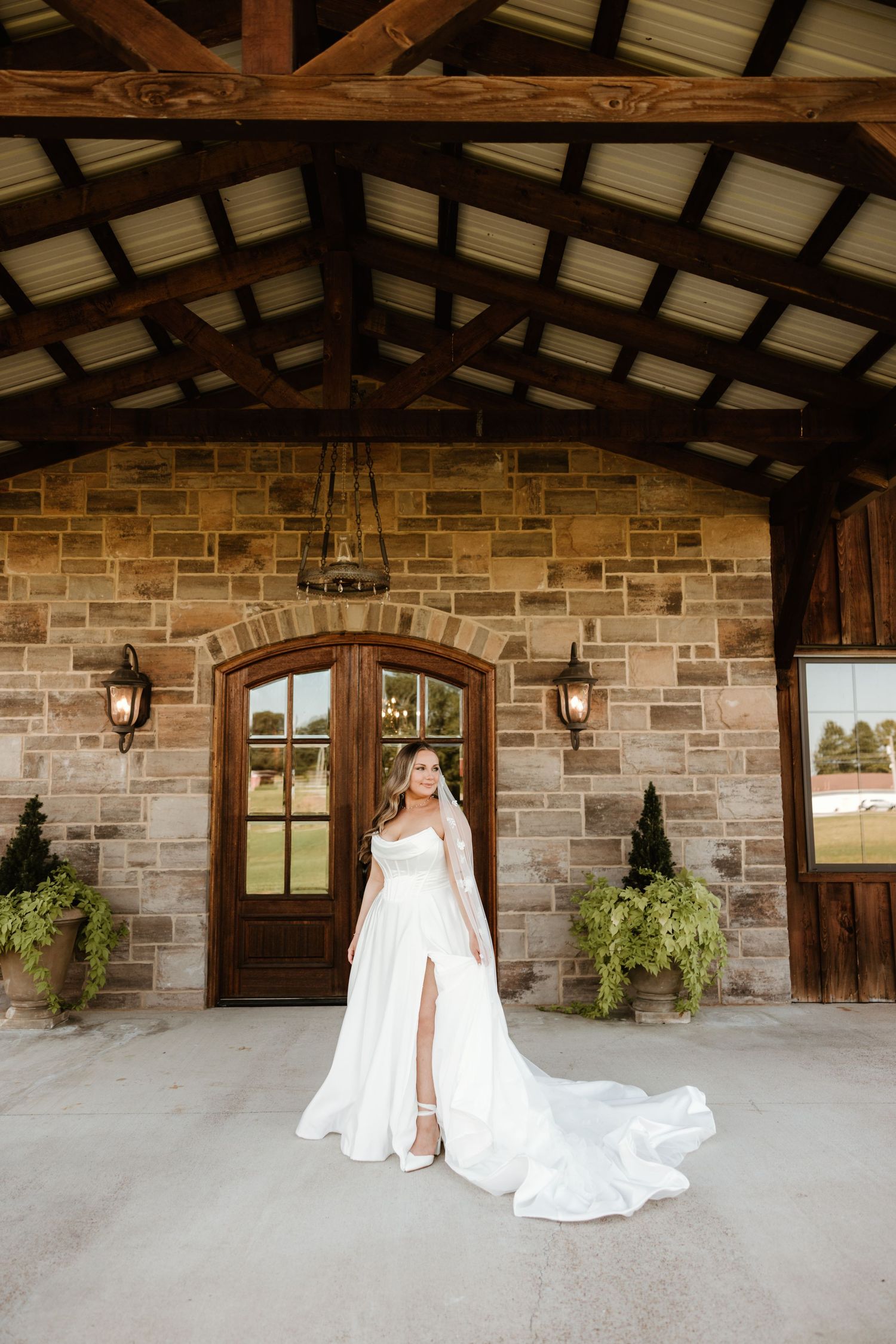 Elegant wedding dress with flowing train photographed in front of rustic stone building with wooden beams and lanterns.