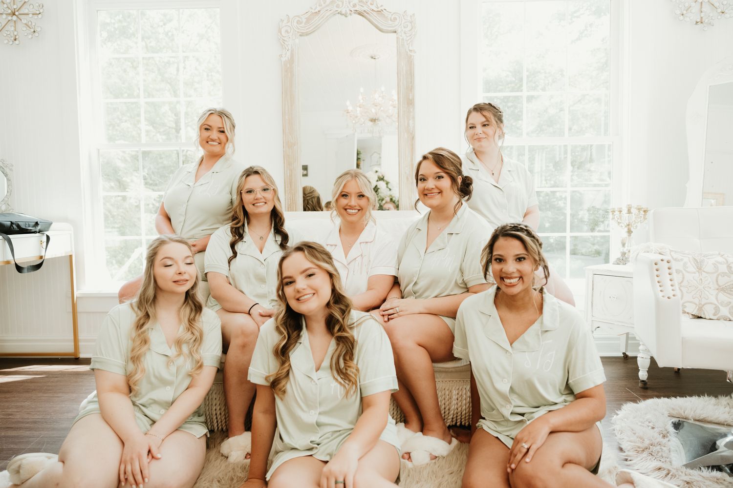 A bridal party wearing matching silk robes poses together on a couch in a bright, elegant white room.