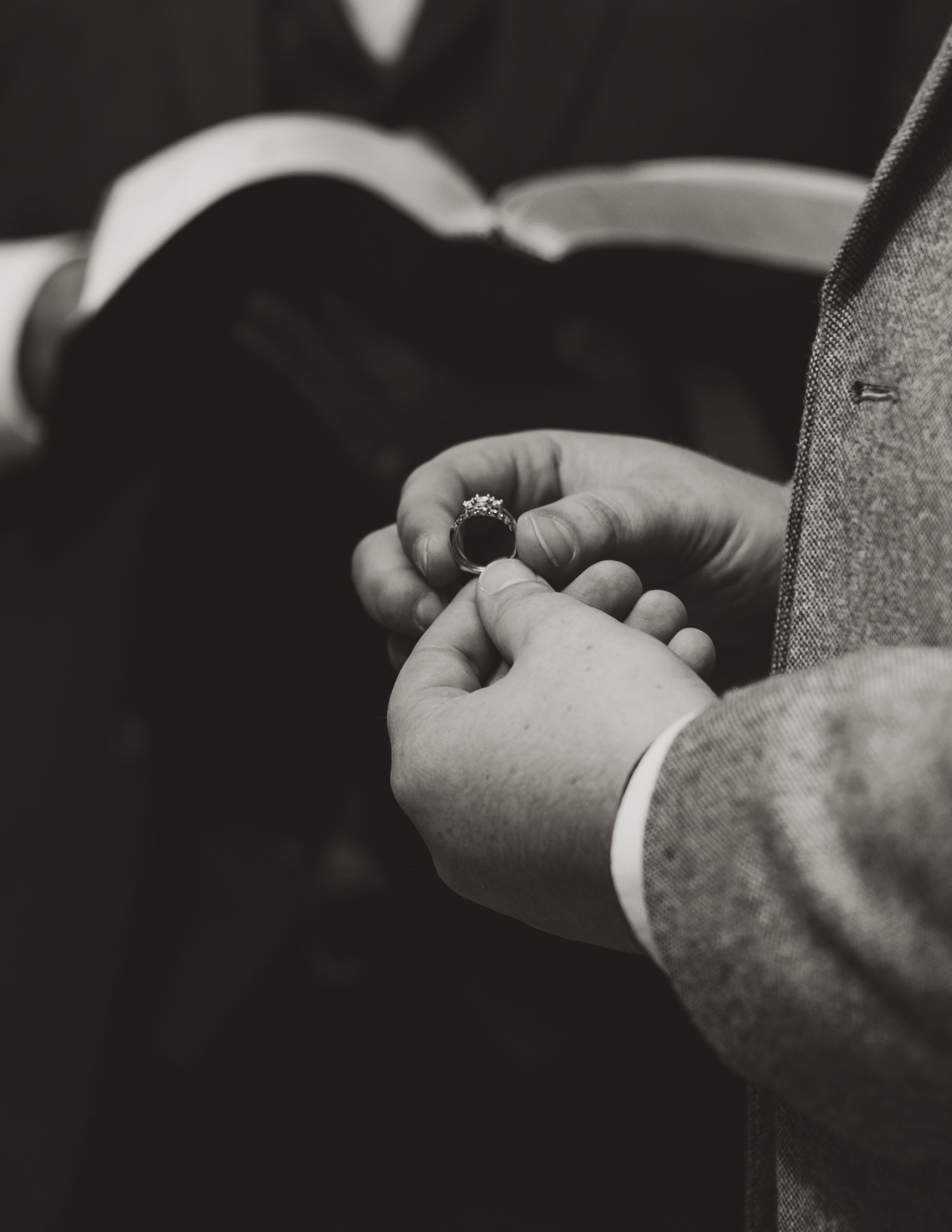 A black and white close-up photograph of two hands exchanging a small ring during what appears to be a ceremony.