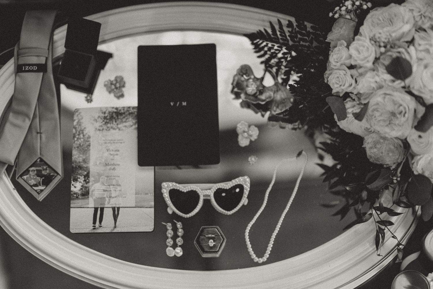 A black and white collage of wedding details including flowers, rings, invitations, and jewelry arranged side by side.