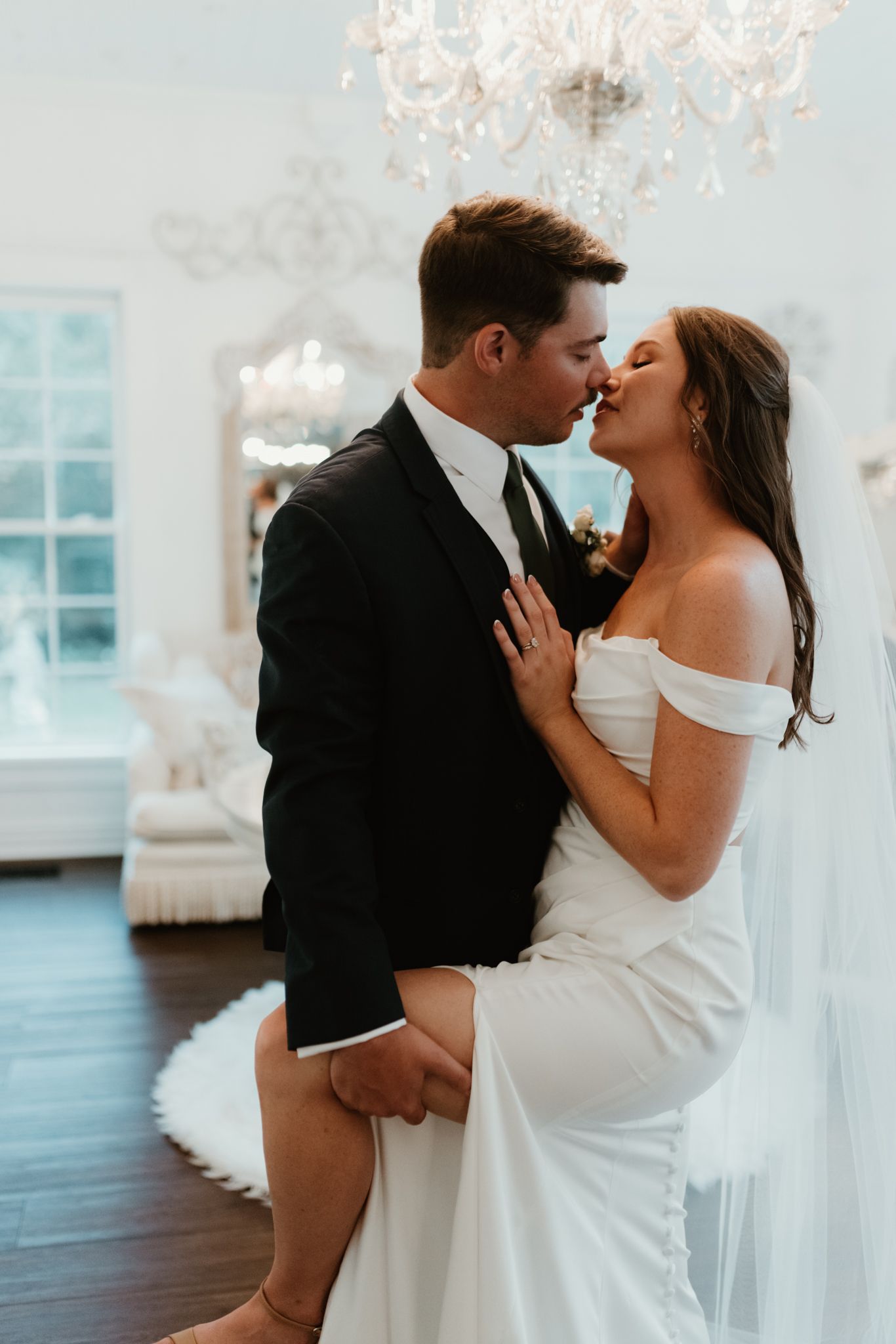 A romantic couple sharing an intimate moment in an elegant white room with a crystal chandelier above.