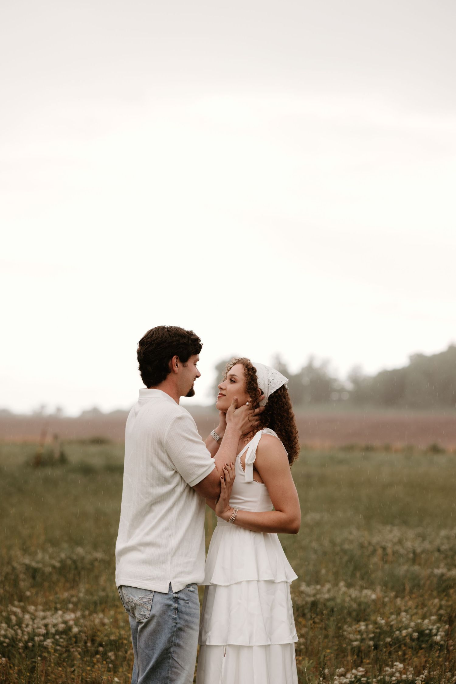 A romantic couple share an intimate moment while standing together in a wildflower meadow at sunset.