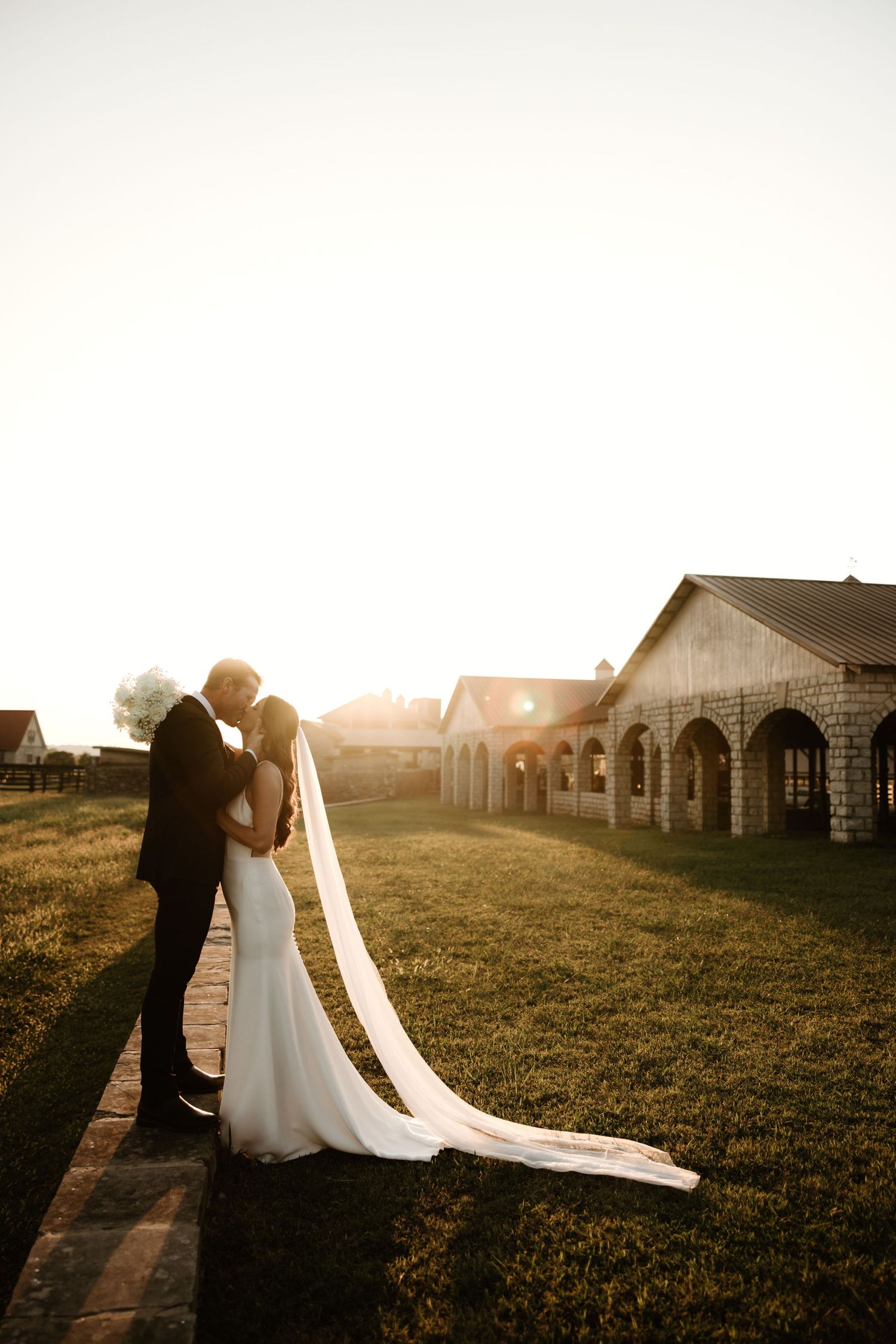 Golden hour wedding photos capture silhouettes and long shadows across a grassy field near historic buildings.