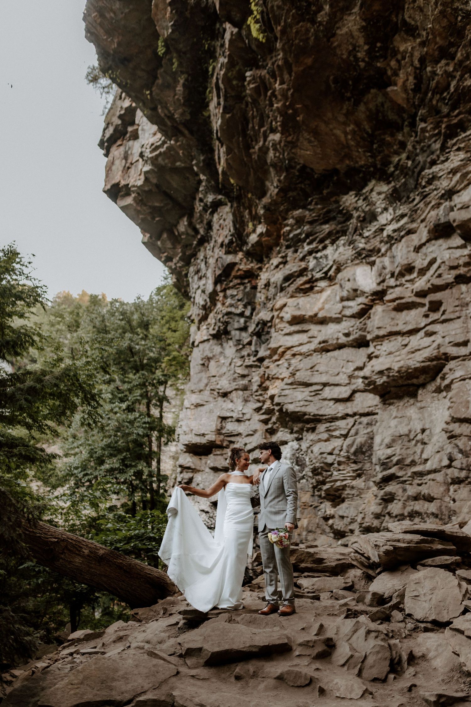 Bride and groom share romantic moment beneath massive layered rock wall during outdoor elopement.