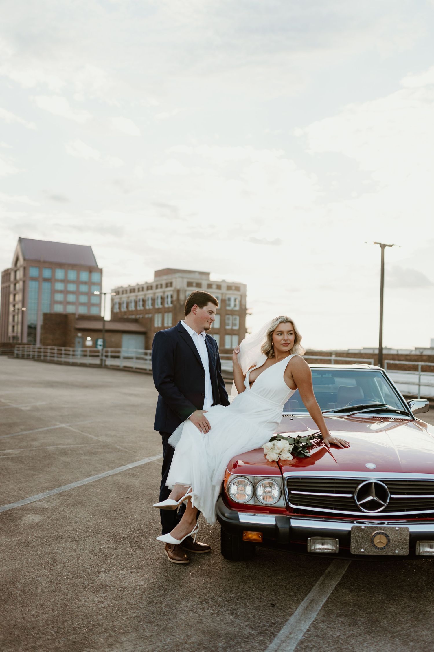 Wedding couple poses with classic red Mercedes-Benz car in an urban setting.