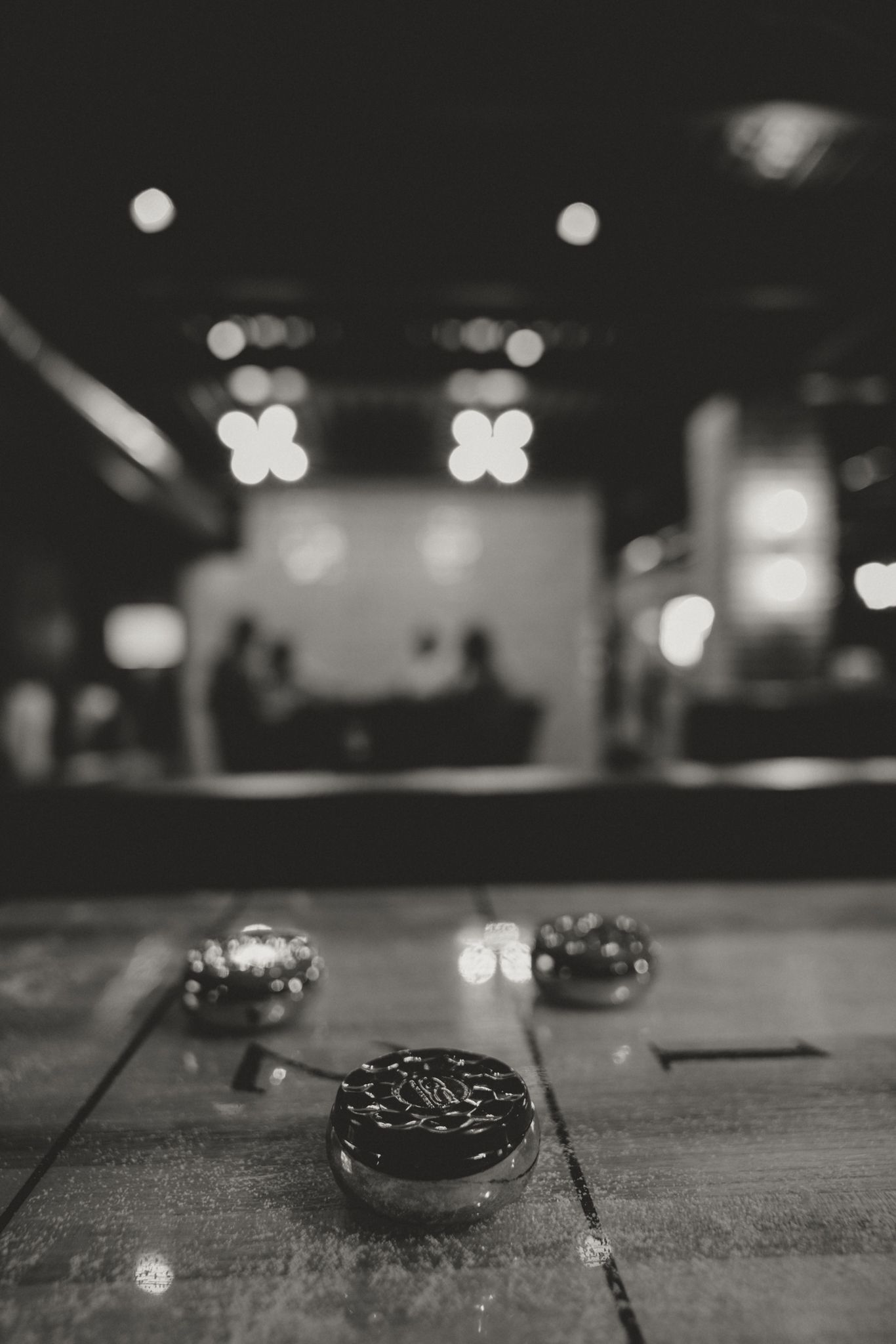 Black and white photograph of decorative objects on a wooden table with blurred bokeh lights in background.