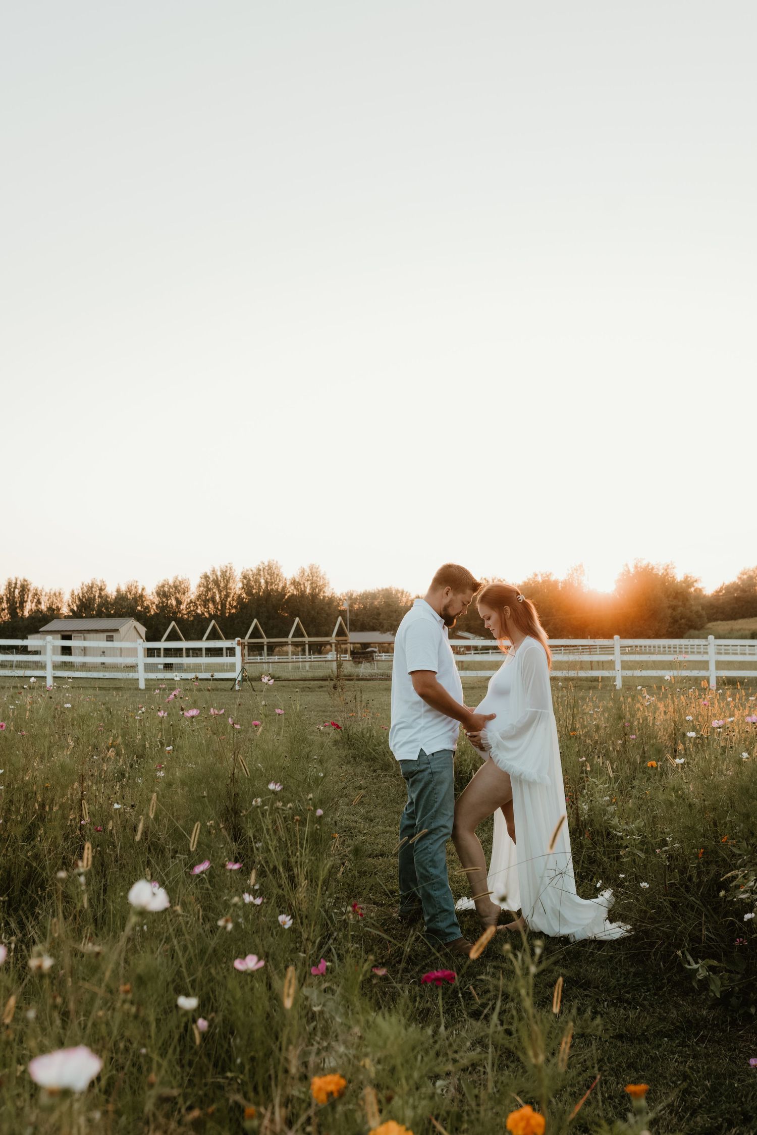 A romantic sunset photoshoot in a wildflower meadow with a white fence in the background.