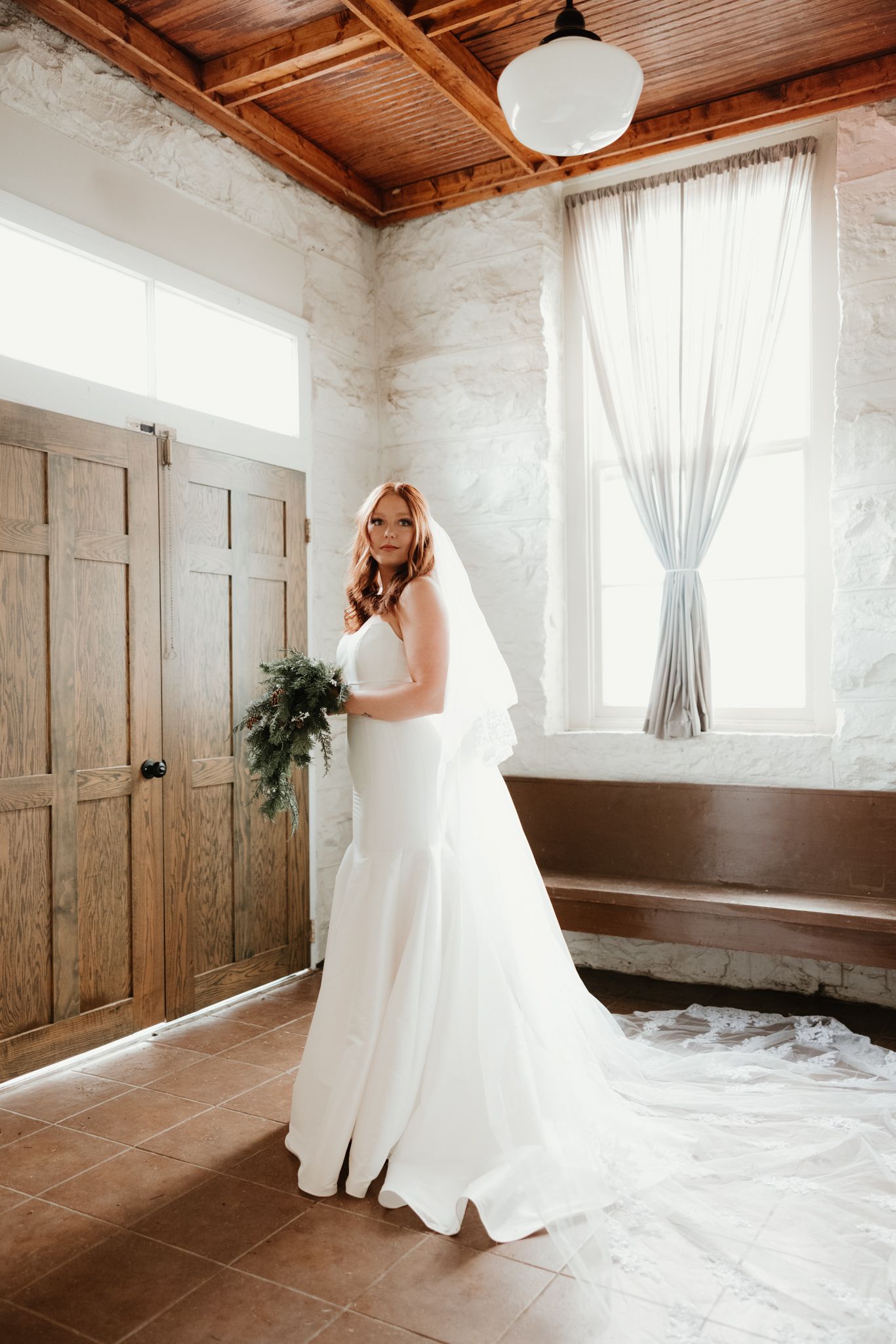 A wedding dress portrait in a sunlit room with wooden doors and white stone walls.