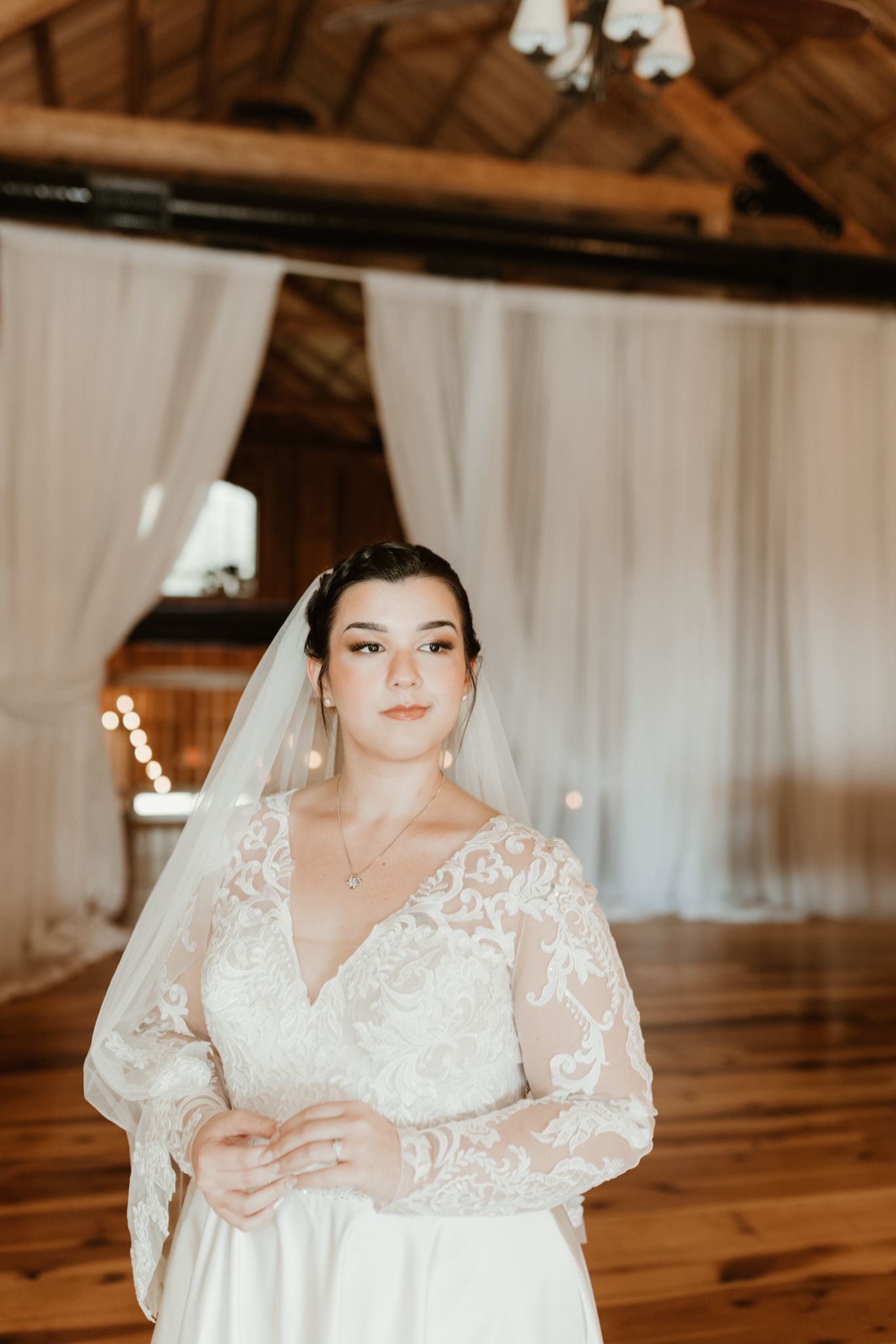 A bride wearing an elegant lace wedding dress with long sleeves poses in a rustic wooden venue.
