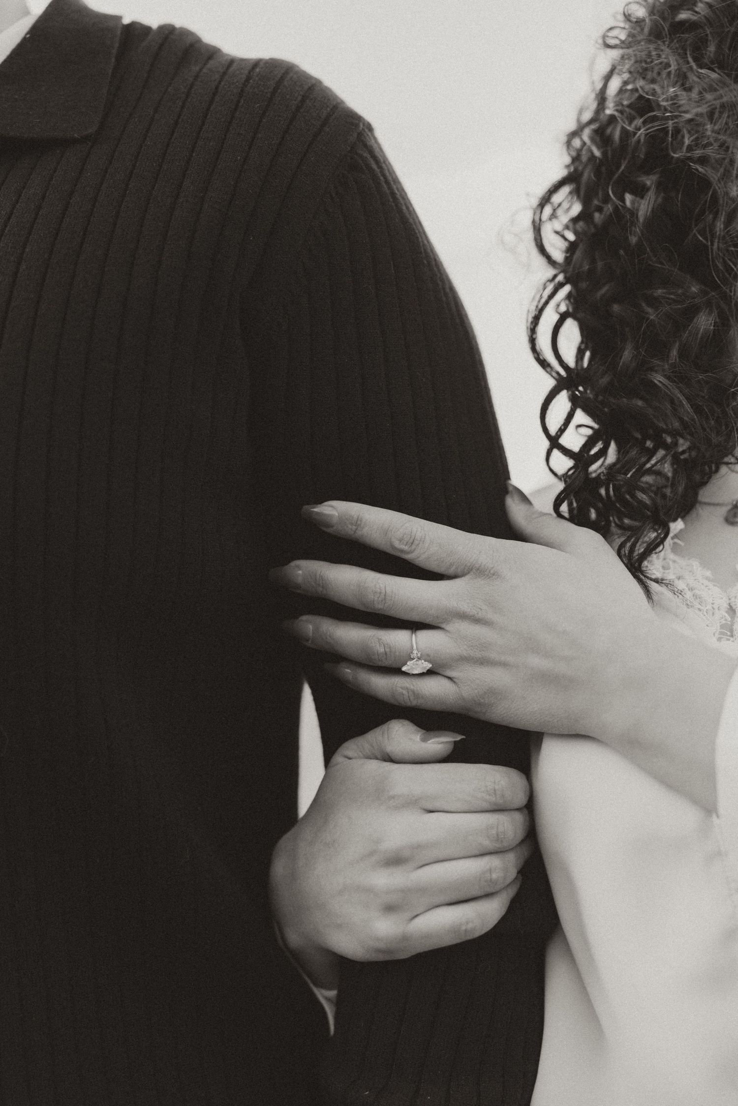 Close-up black and white photo showing hands with engagement ring against sweater texture.