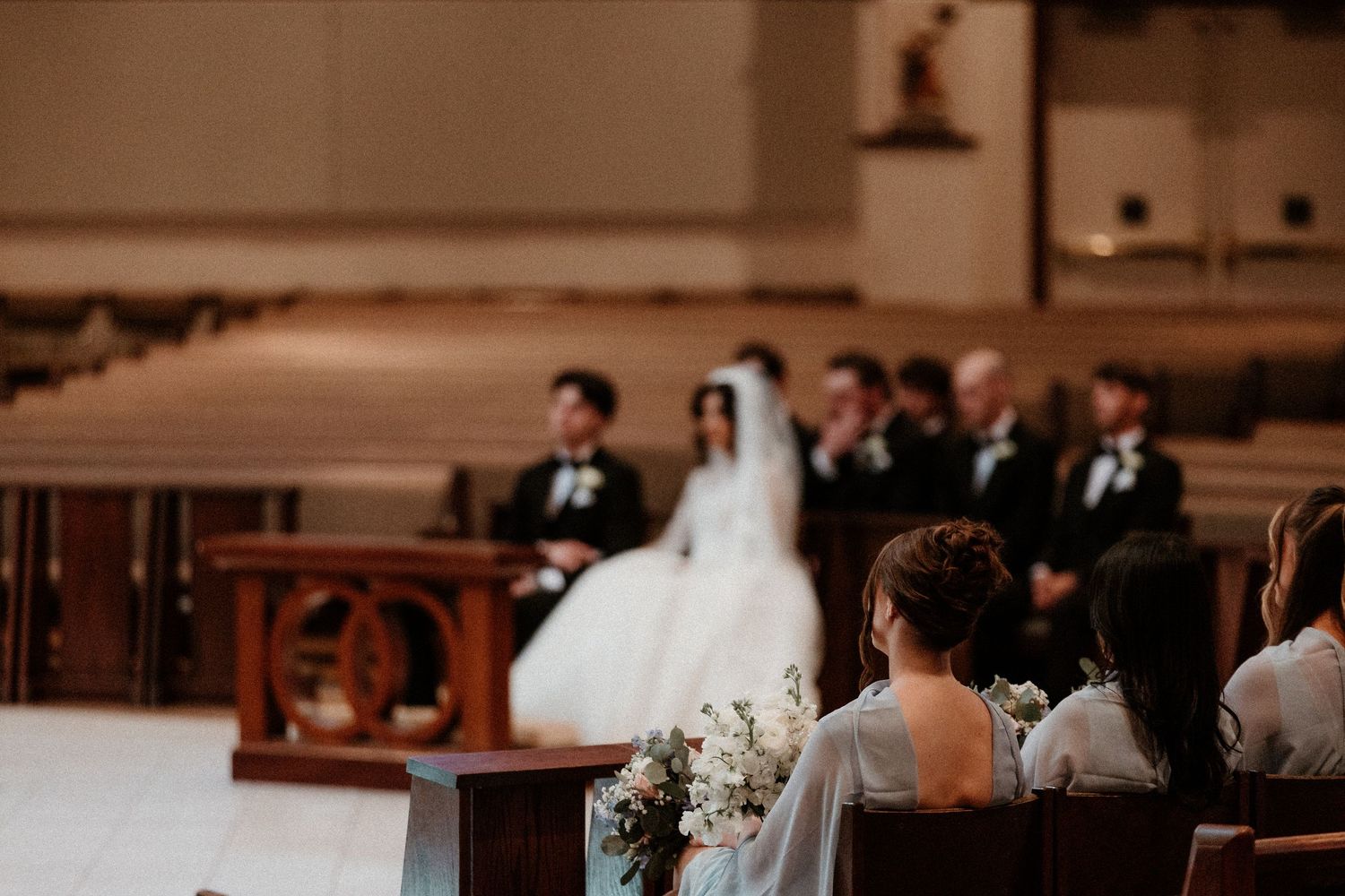 Bride in white gown stands at church altar during wedding ceremony with guests seated in pews.