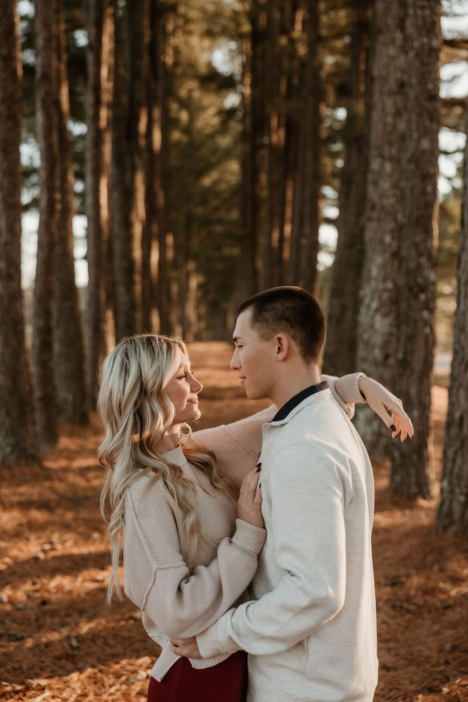 Couple embracing and gazing at each other in a pine forest with warm autumn leaves on the ground.