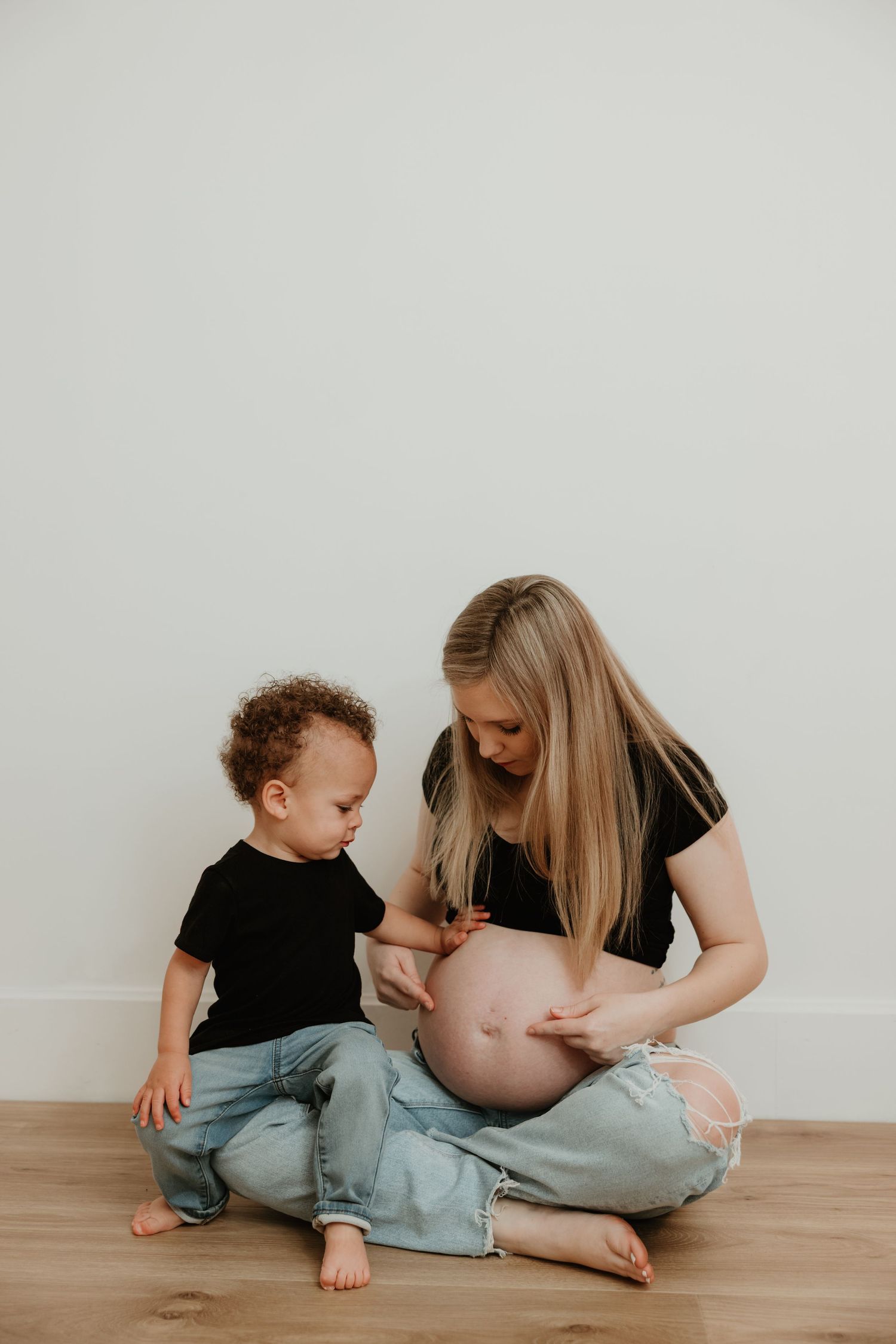 An indoor maternity photo with a young child looking at a growing baby bump.