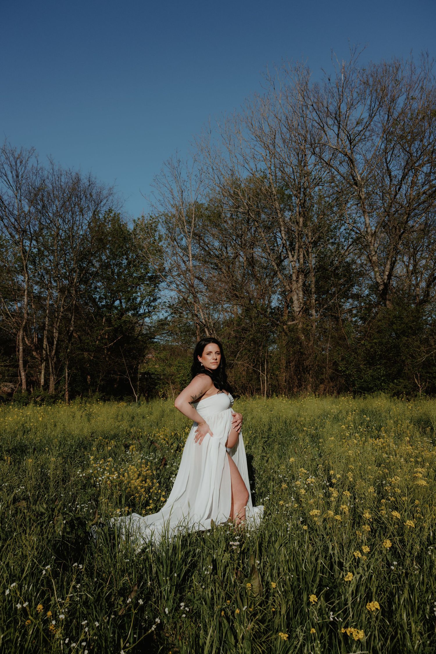 A maternity portrait in a flowing white dress amid a field of yellow wildflowers.