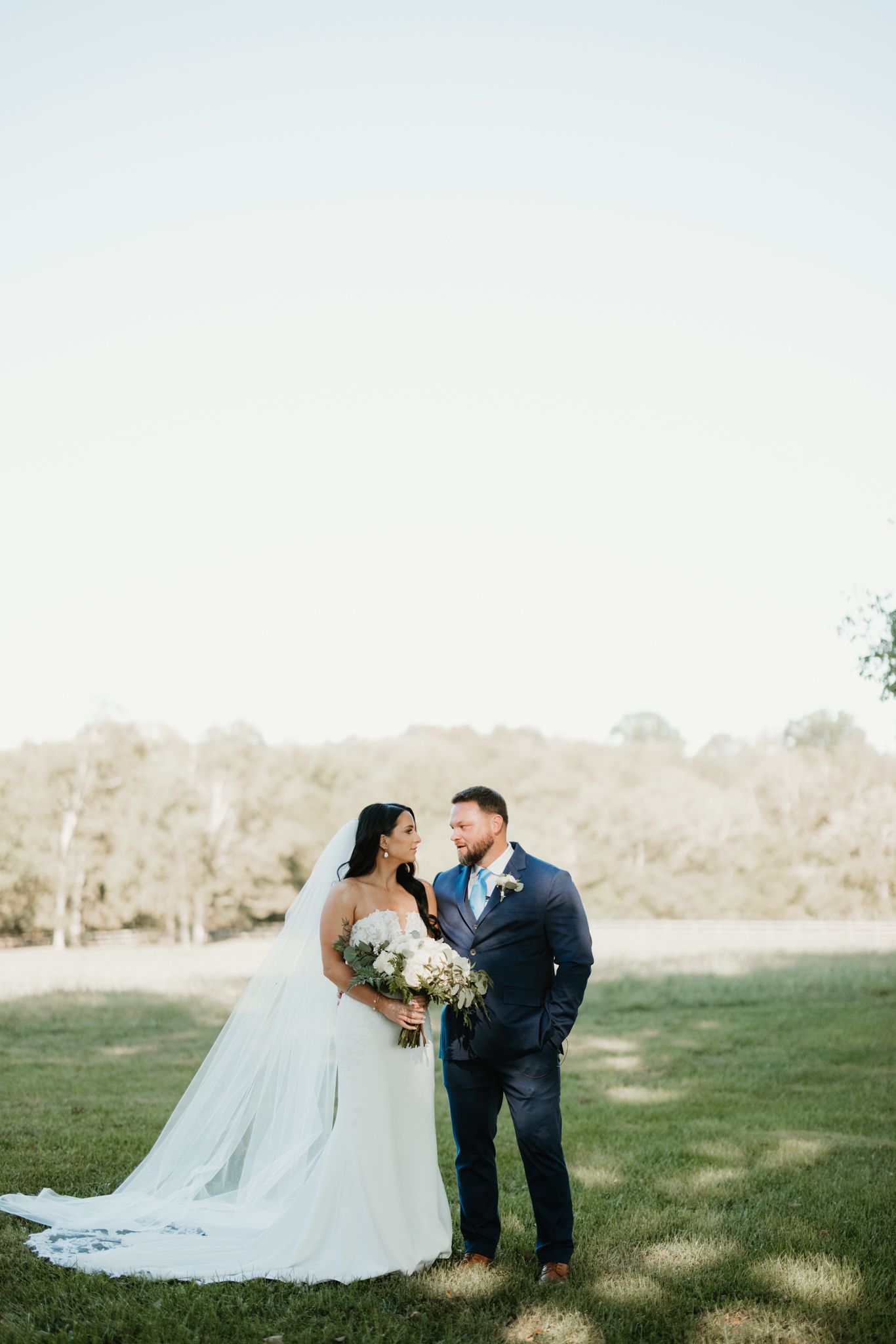 Wedding couple poses in an open grassy field on their special day.