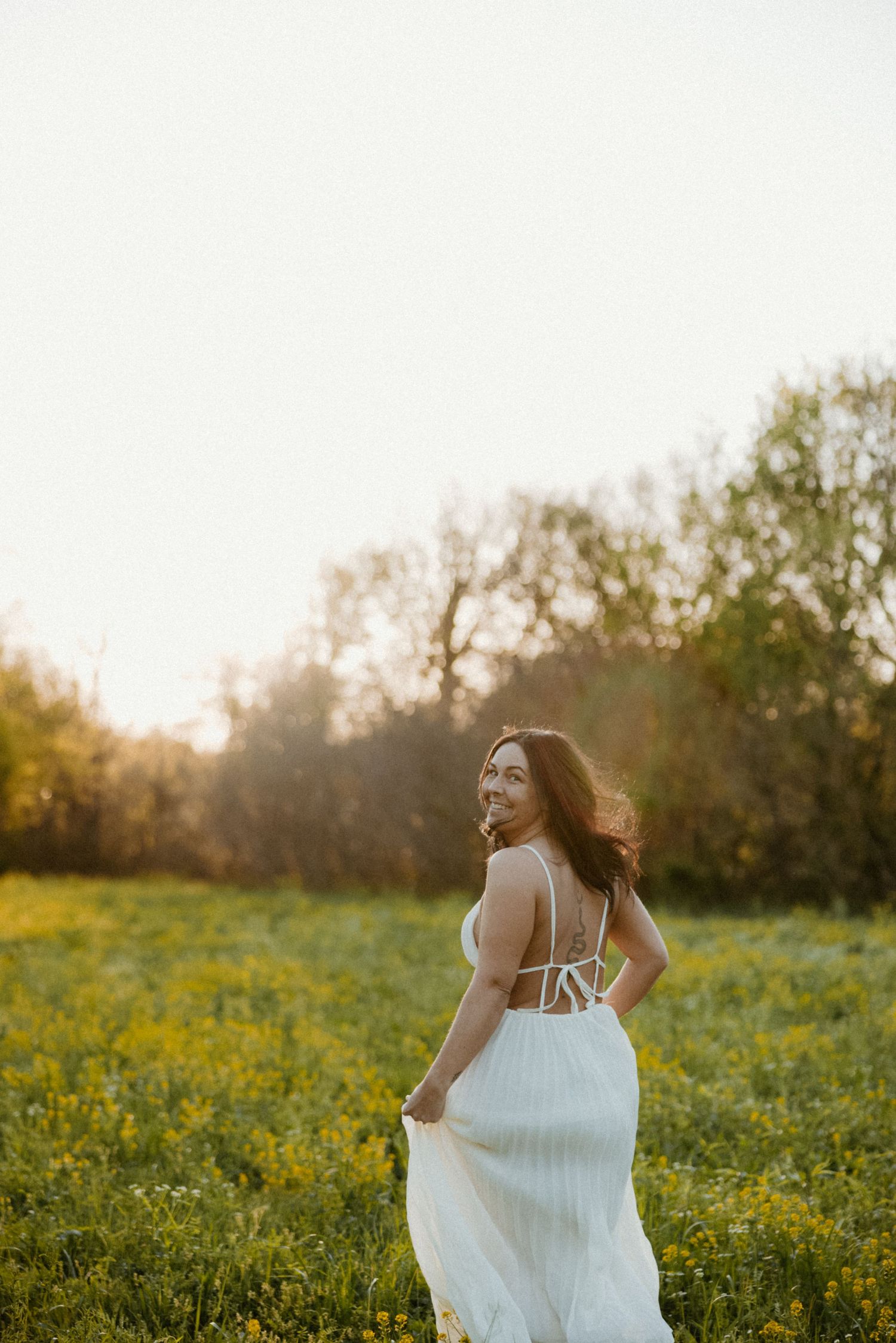 Woman in white dress twirls in sunlit meadow of yellow wildflowers.
