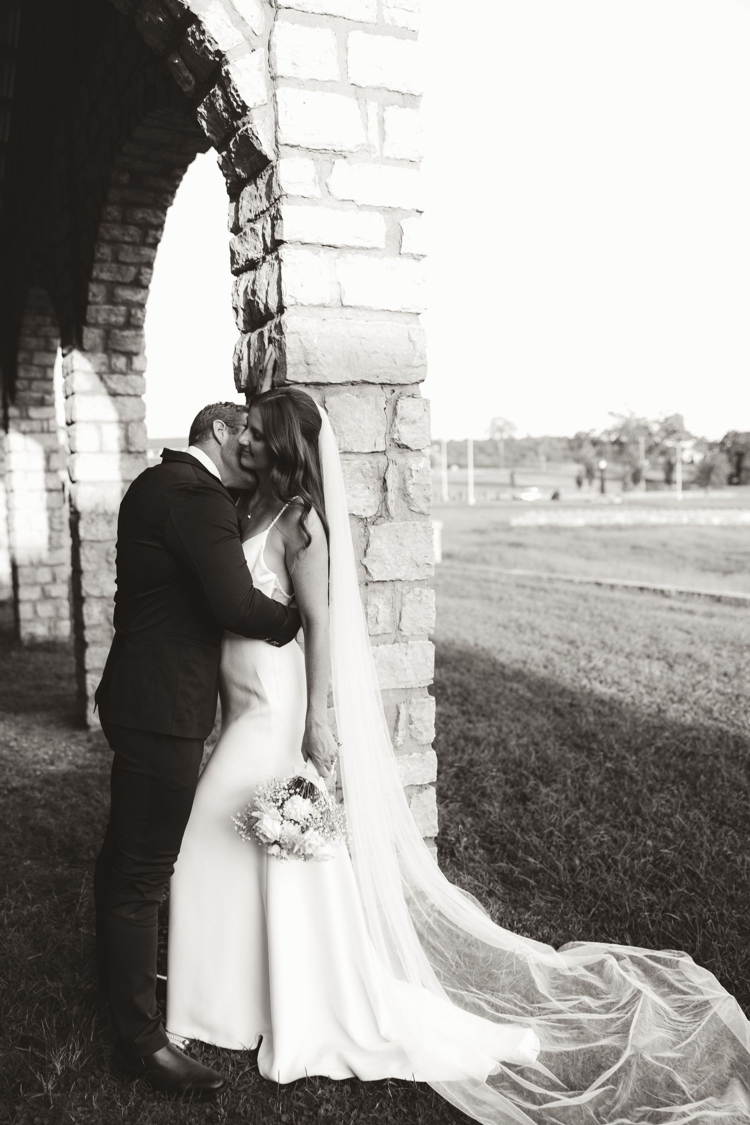 Wedding couple shares intimate poses by white stone pillars in a romantic black and white photoshoot.