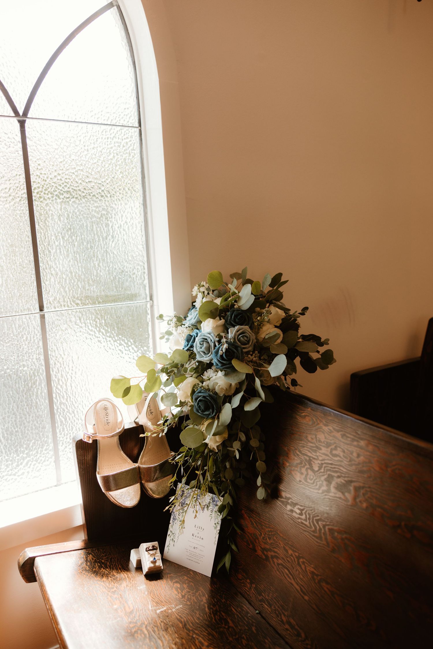 Delicate floral arrangement with blue and white roses against a dark wooden surface next to a sunny window.