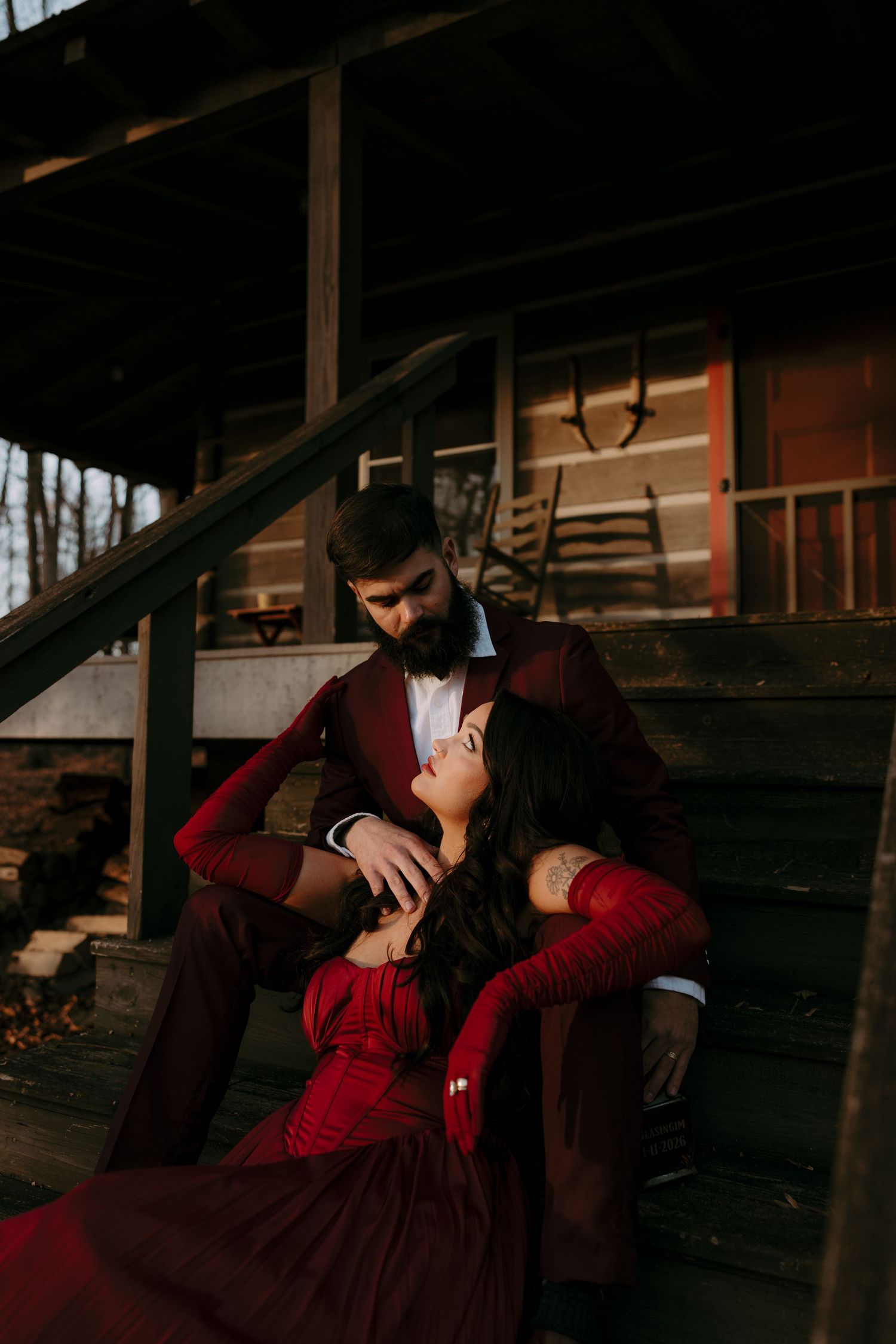 Couple in matching red outfits sitting on rustic cabin steps, woman leaning back on man in romantic pose.