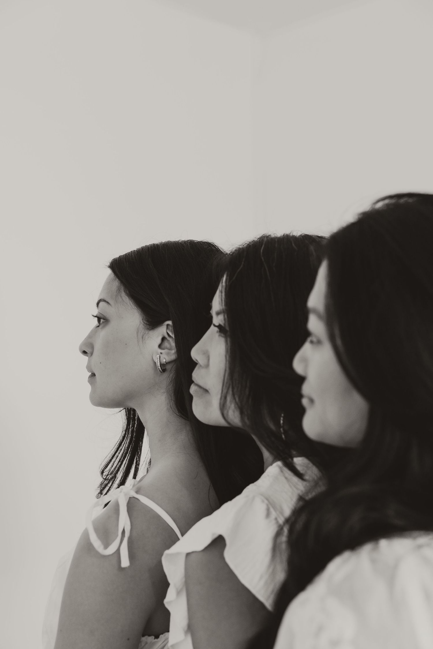 Black and white profile portrait of three young women with dark hair standing in a row against a light background.