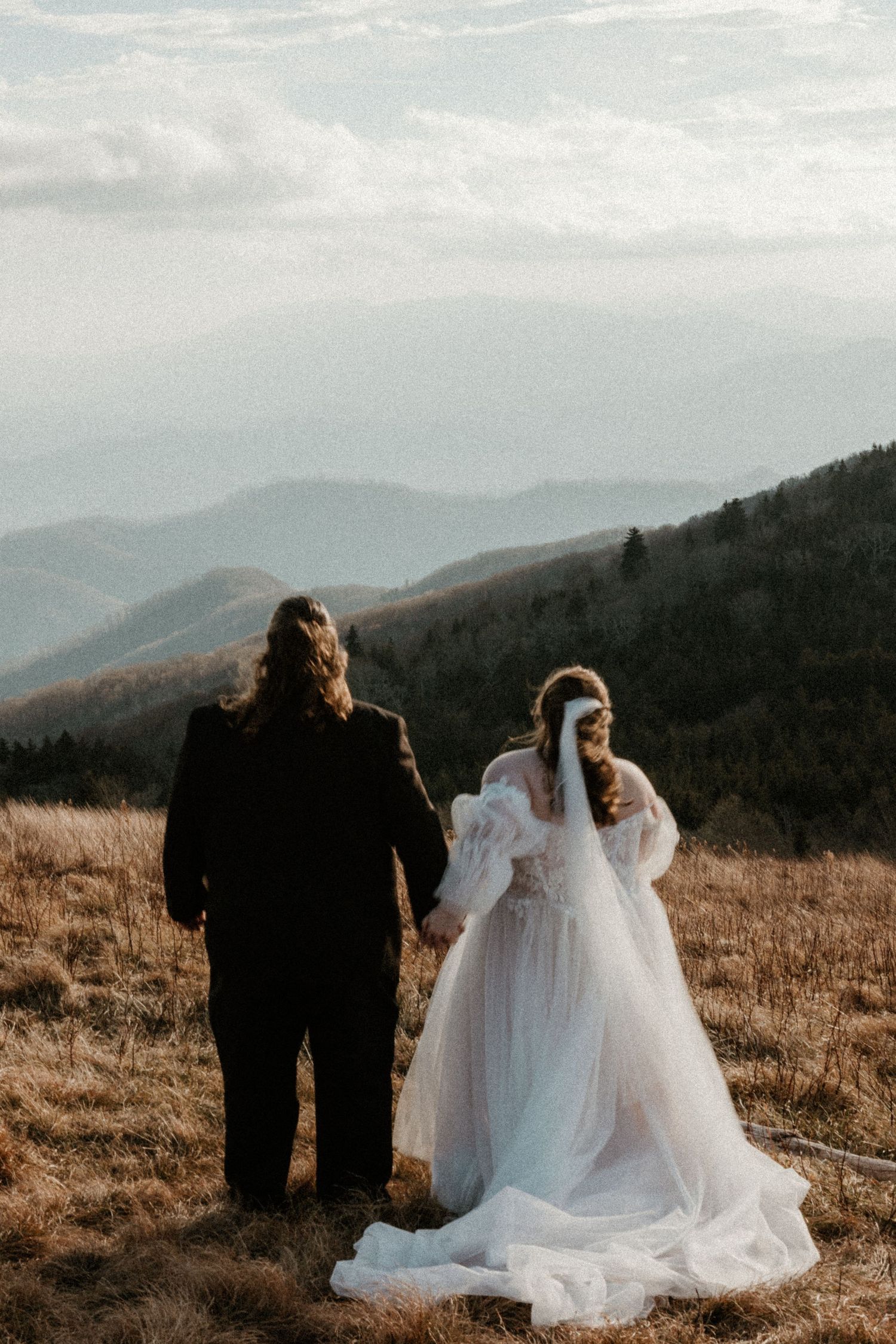 Bride and groom holding hands while overlooking stunning mountain landscape during outdoor elopement ceremony.